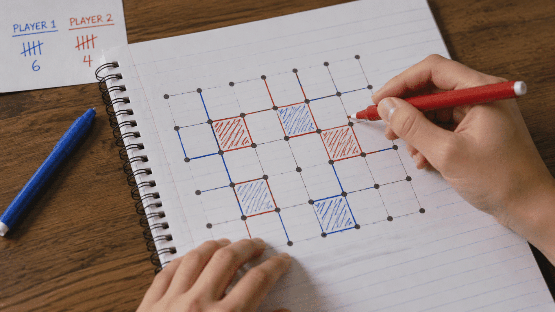 hand with a red marker playing dots and boxes game on a spiral notebook