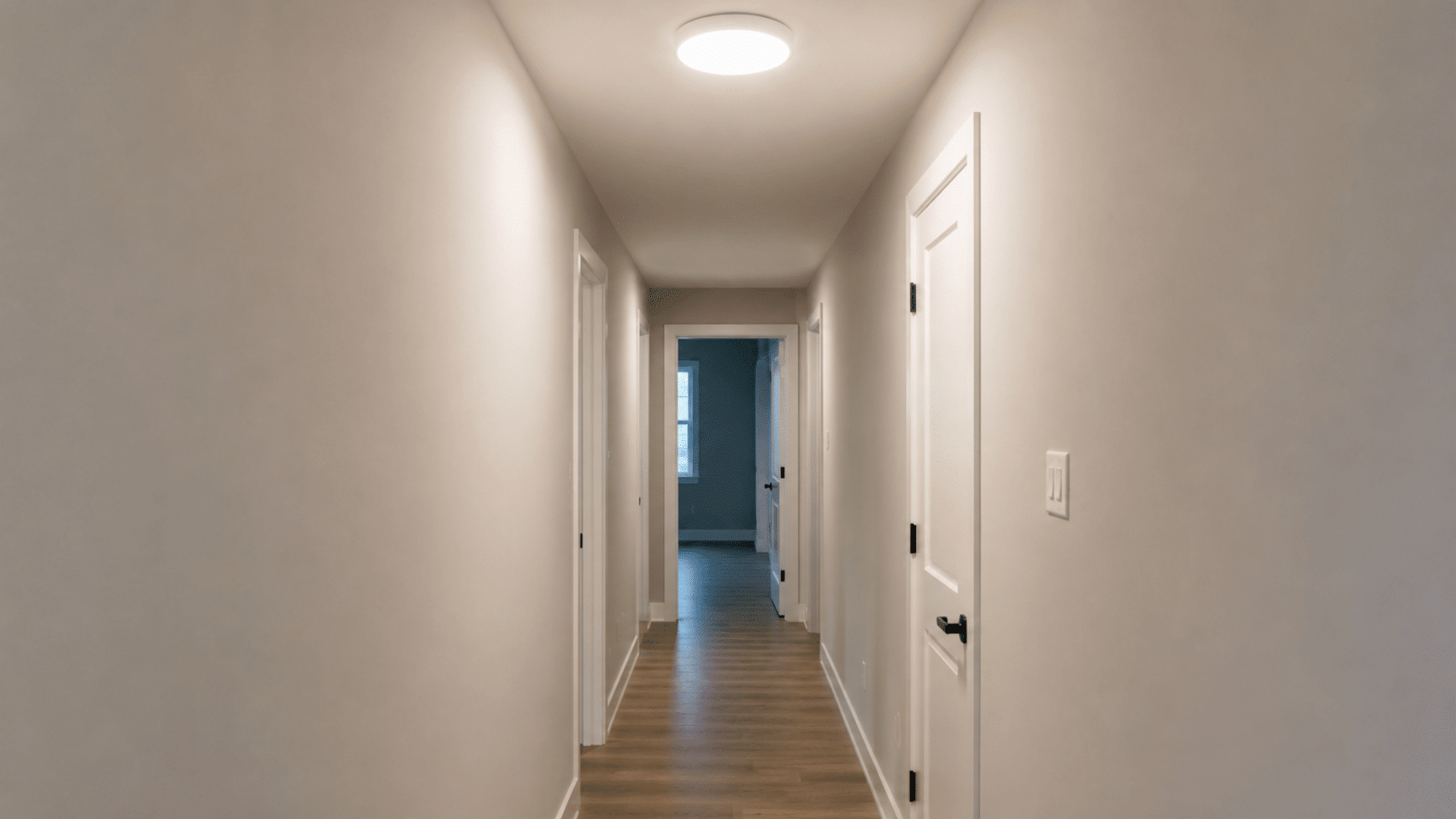 interior photo of a flush mount ceiling light sitting flat against the ceiling of a narrow hallway the fixture has a simple round enclosed white or light metal cover with no drop gap