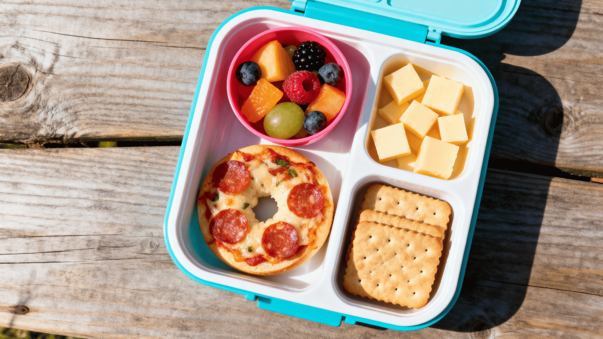 blue kindergarten lunchbox with a bagel pizza, fruits, cheese cubes and crackers