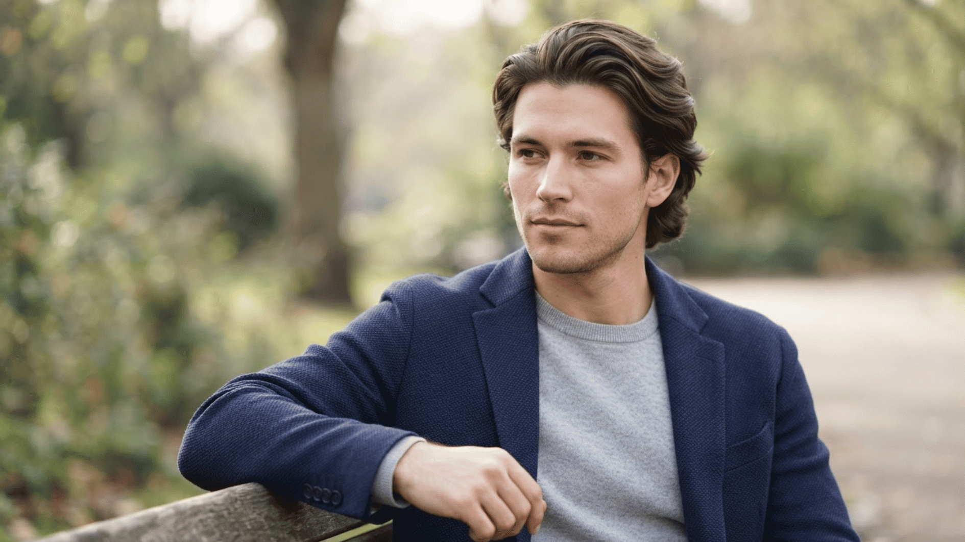 man with medium length flow haircut outdoors wearing blazer with textured swept back hair style