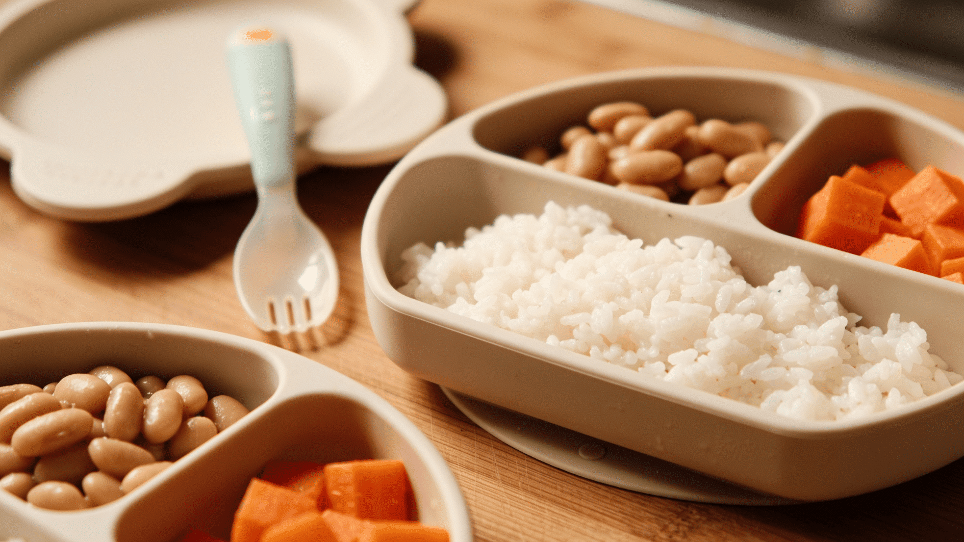 meal prep bowls with rice, soft beans, and steamed carrot pieces, small spoon and child-safe plate nearby