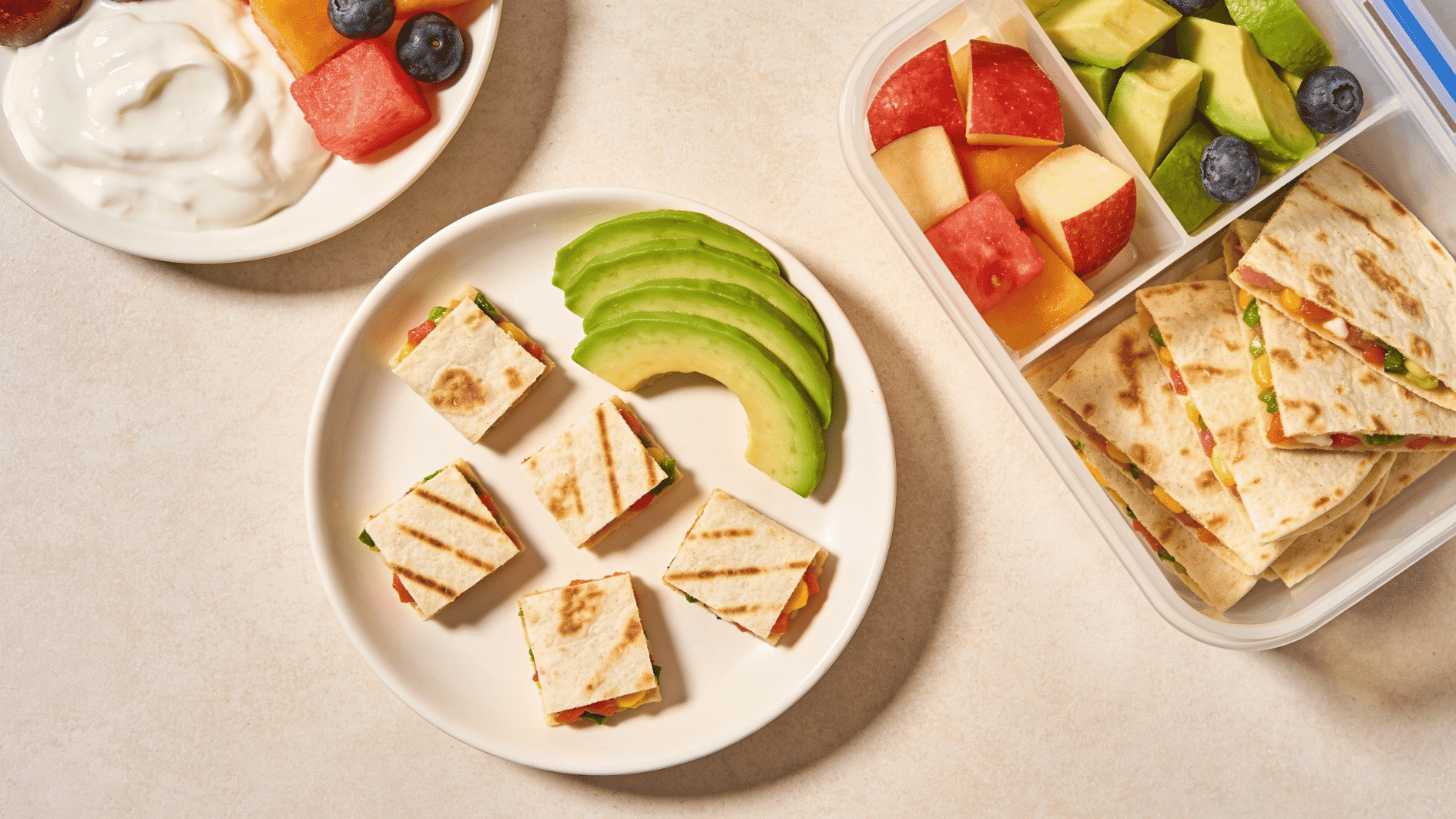 mini quesadilla strips cut into toddler-friendly pieces with avocado, fruit, and yogurt on a small plate