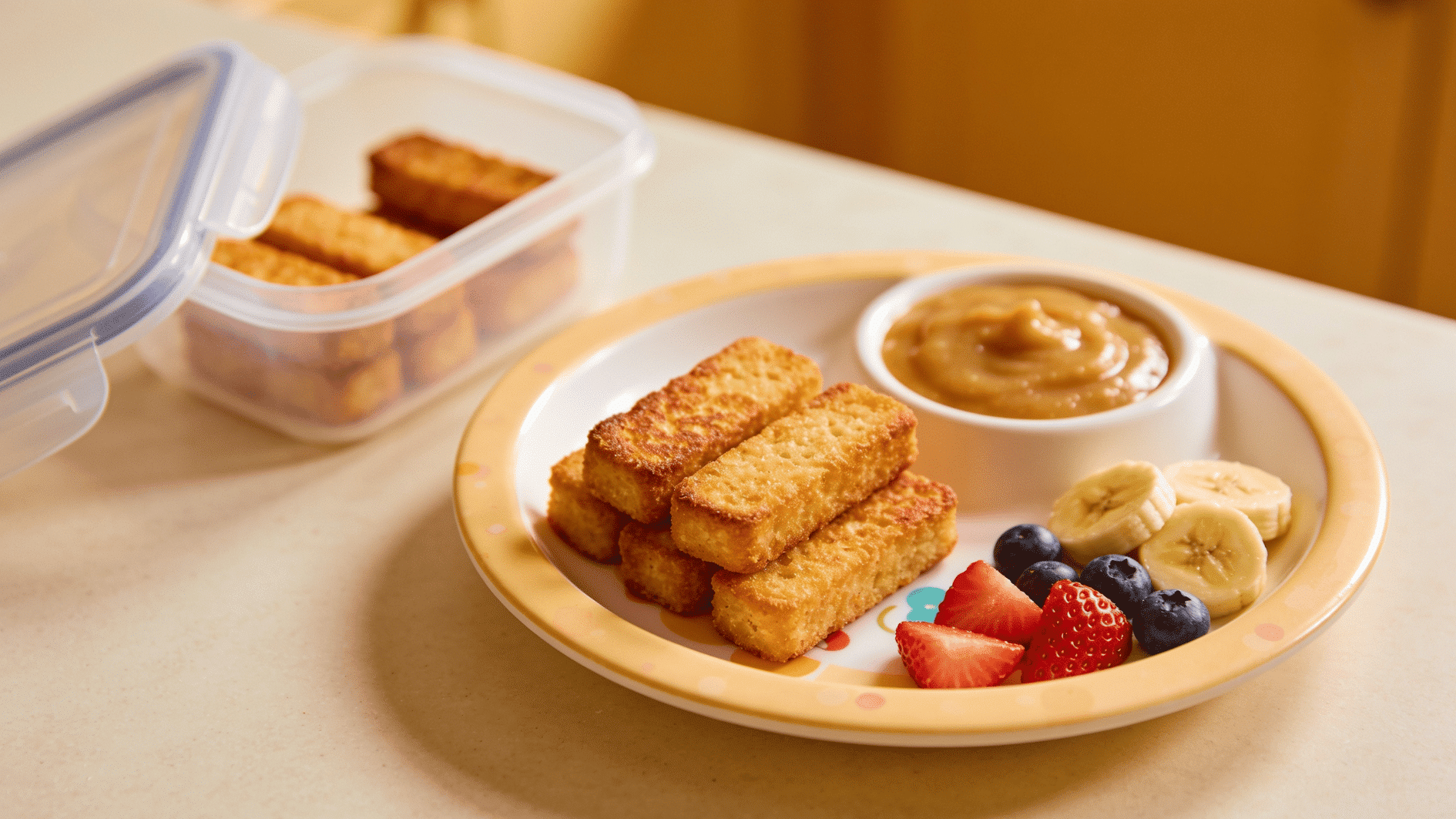 oddler-friendly french toast sticks on a small plate with applesauce dip and fruit piece