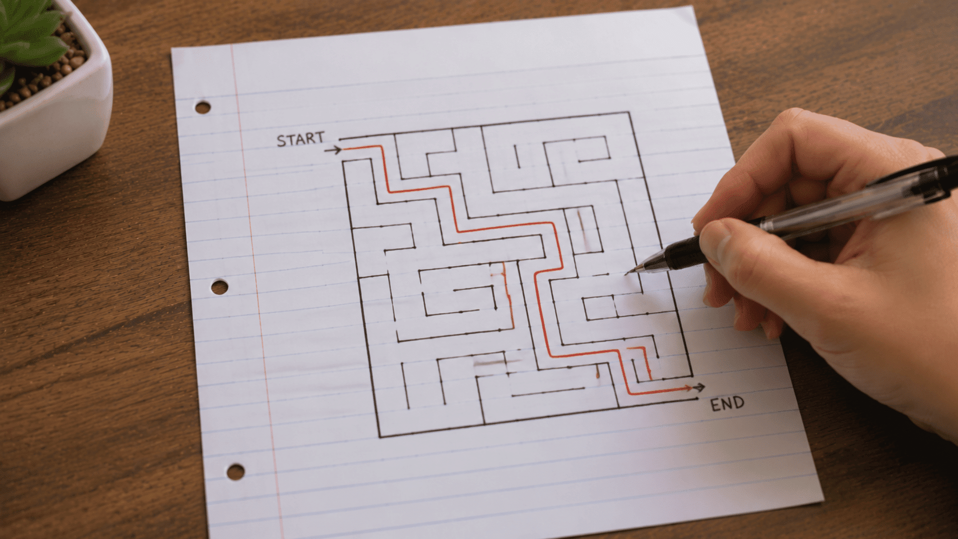 pen tracing a path through a square maze drawn on lined paper from start to end with a solved red line