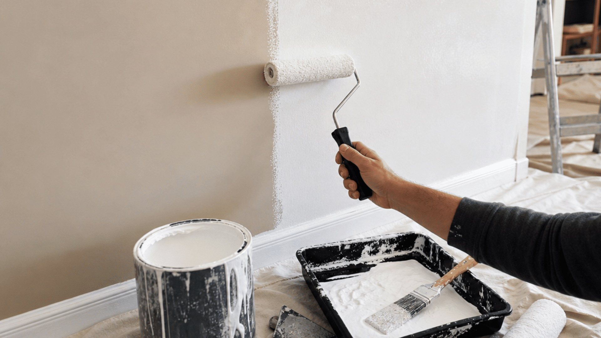 person painting a wall with roller and white paint showing an ongoing home improvement project with tools nearby
