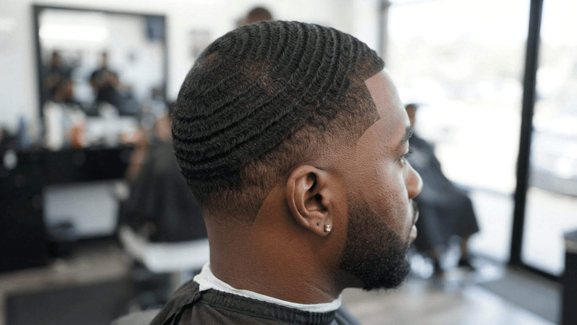 short low fade haircut with defined waves and clean sides shown from side view in barber shop setting
