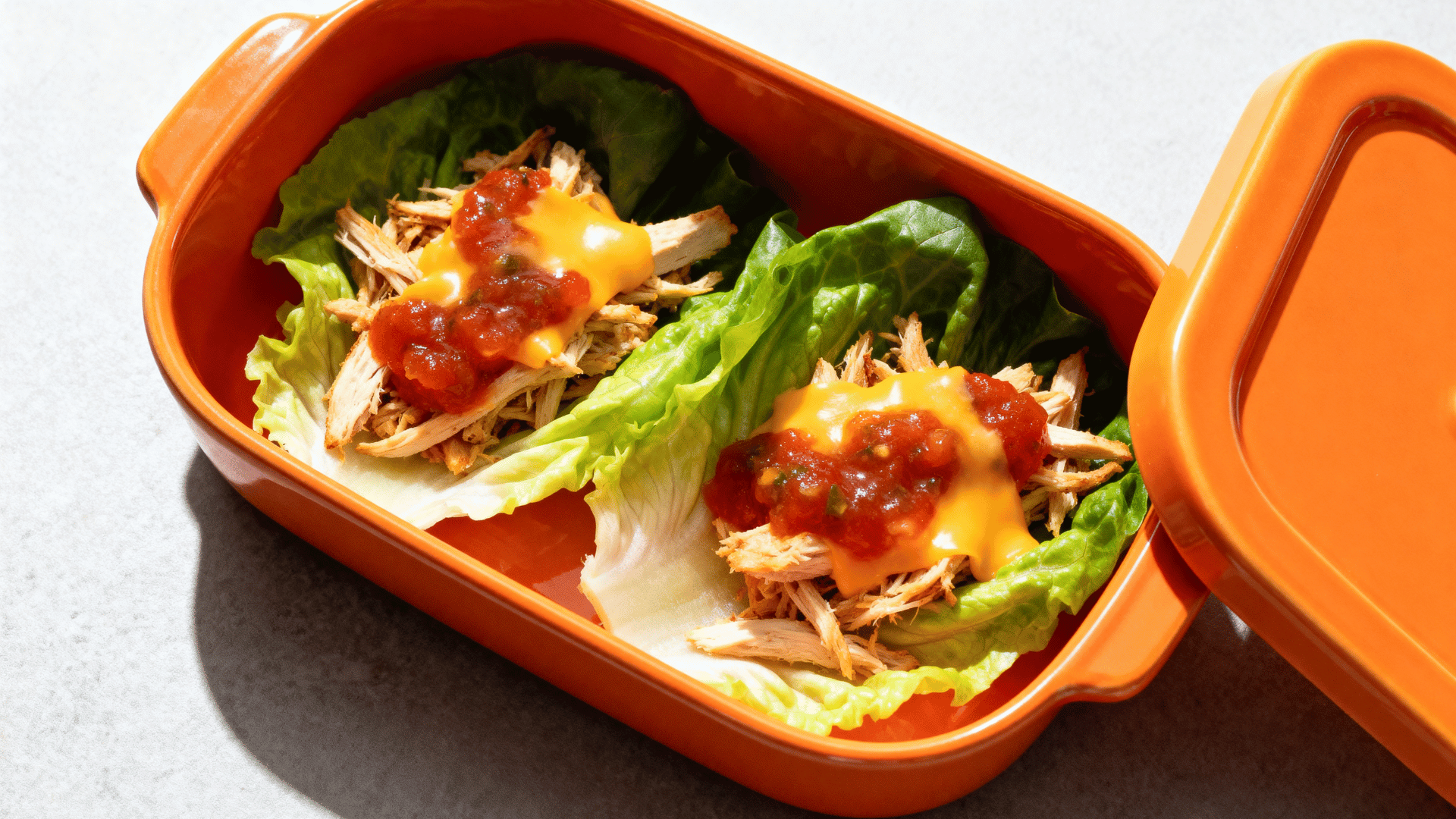 shredded chicken taco lettuce cups in a papaya-orange ceramic lunchbox