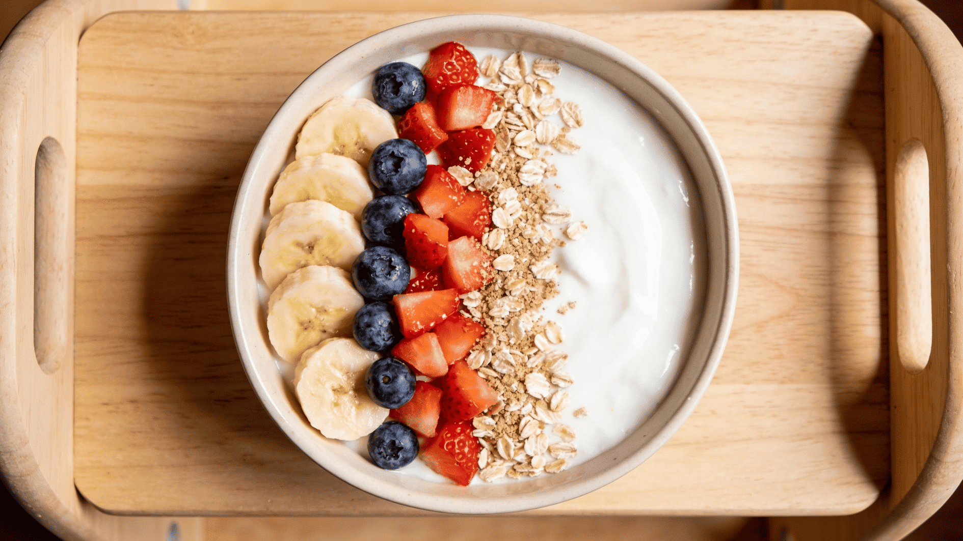 small shallow bowl of thick plain whole-milk yogurt topped with sliced banana, blueberries, and diced strawberries, sprinkled with ground oats,