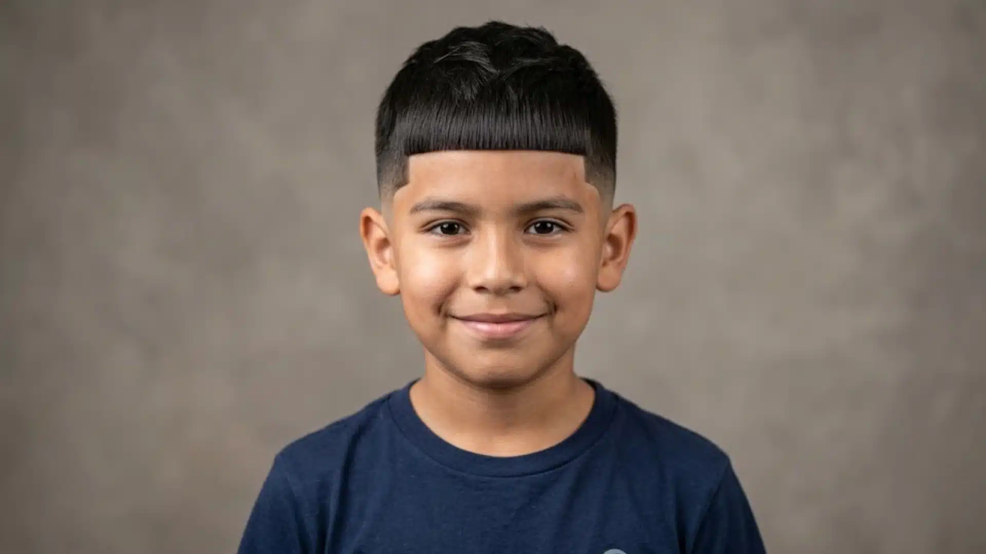 smiling young boy with an edgar haircut featuring a blunt straight fringe and clean faded sides