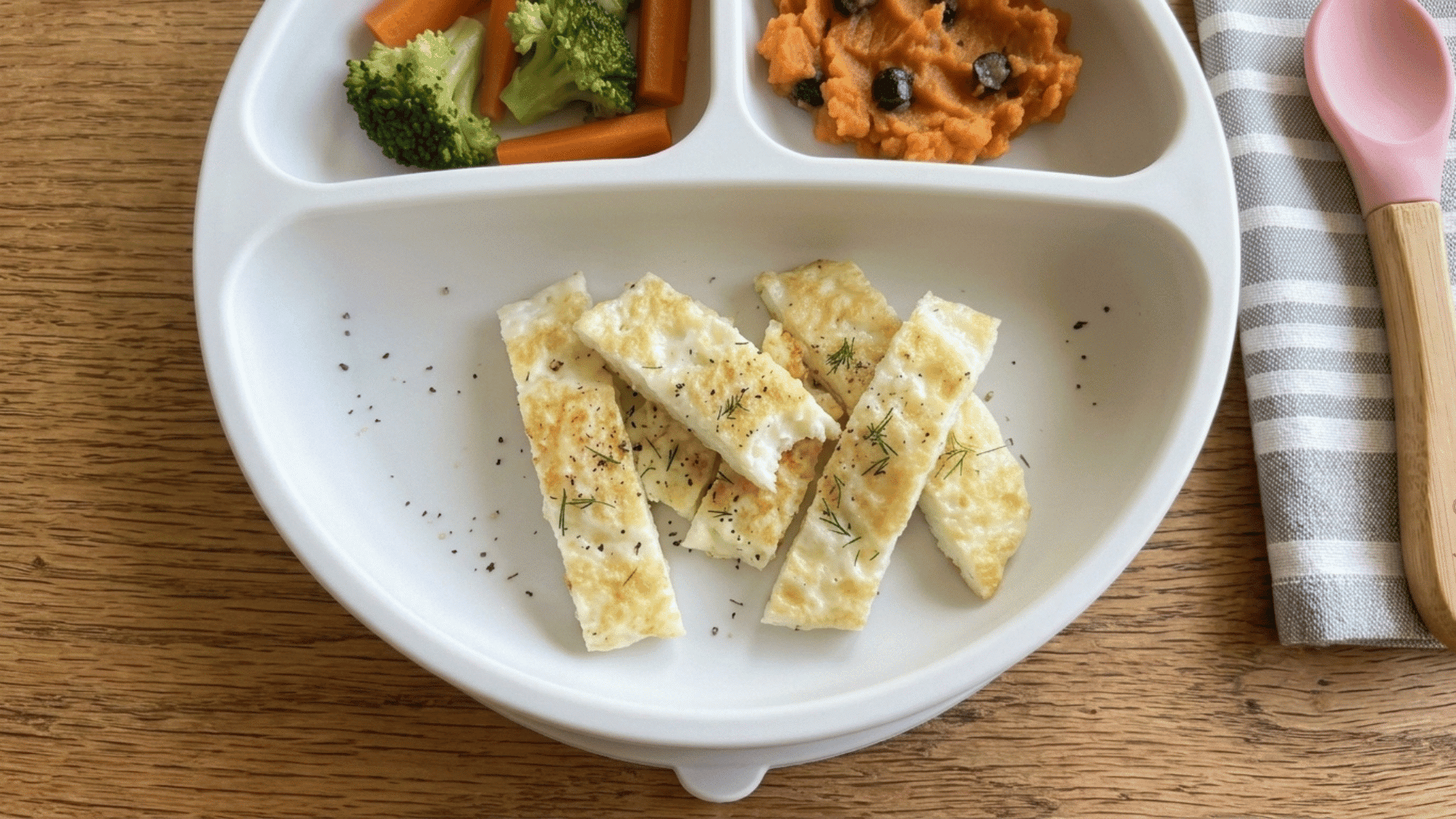 soft-boiled egg white strips with jammy yolk on a white suction plate for baby led weaning