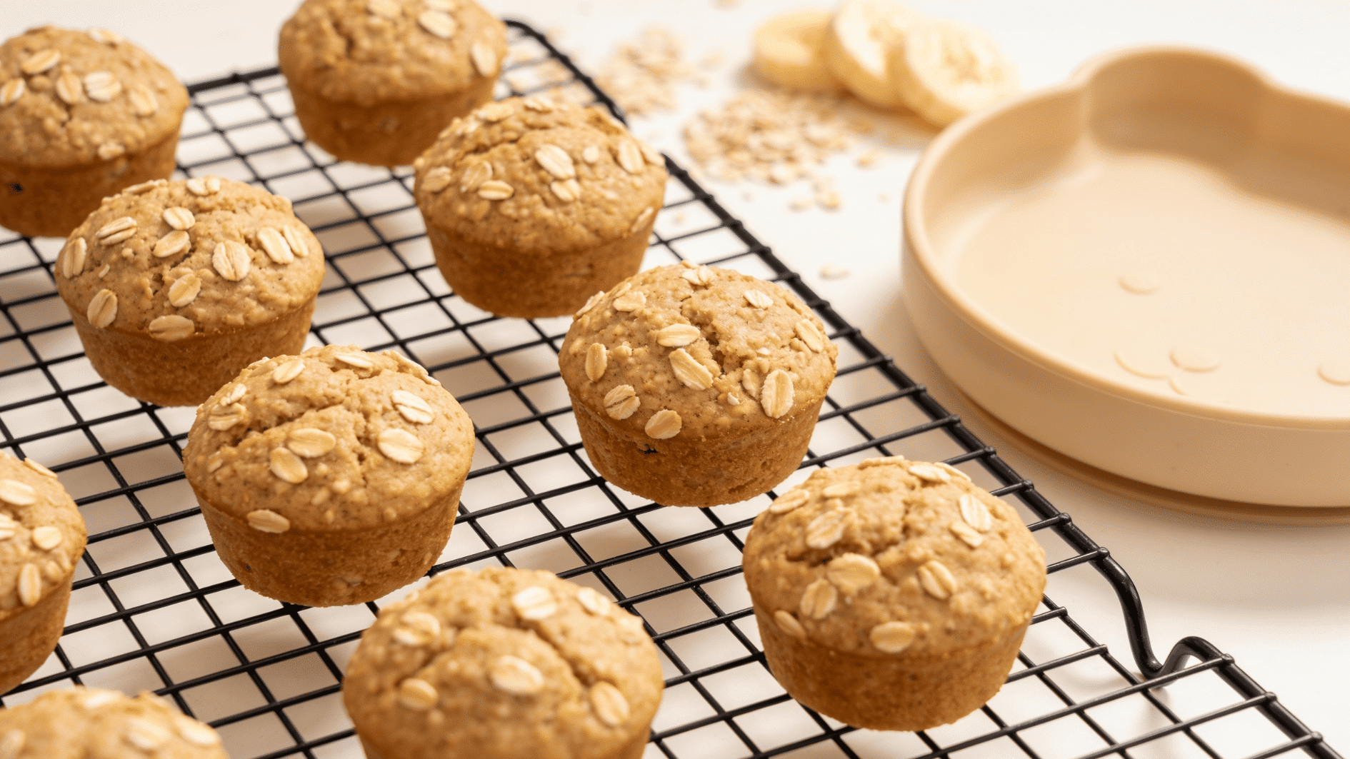 soft mini banana oat muffins cooling on a rack beside a small toddler plate,