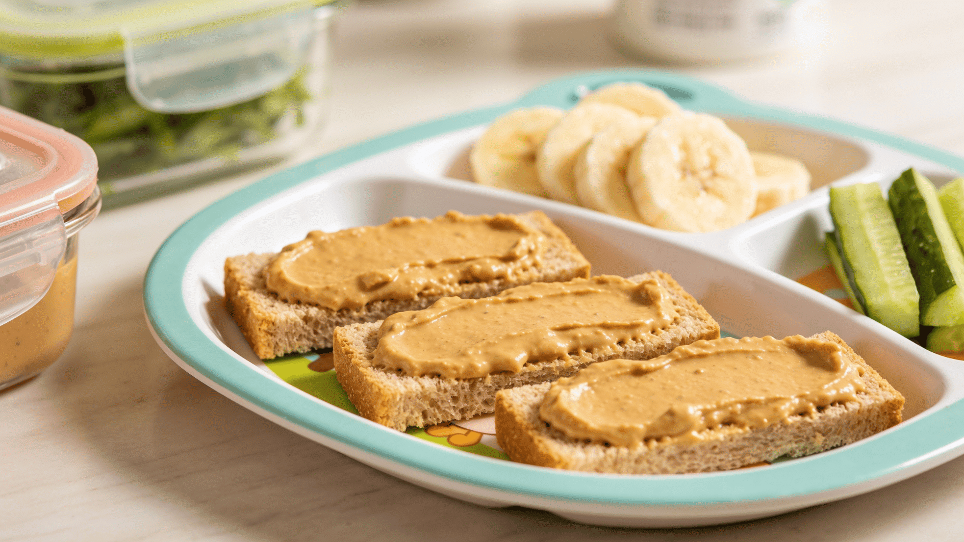 _soft toast strips spread with smooth hummus, served with banana slices and cucumber sticks on a toddler plate