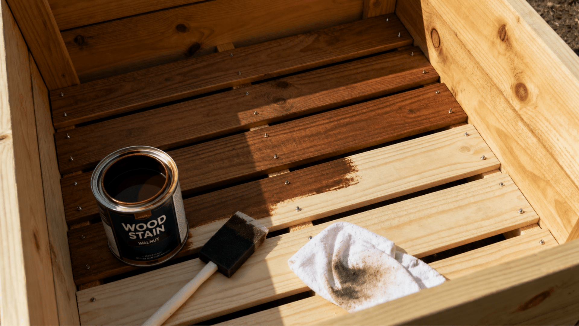 wooden planter box being stained with walnut finish using a foam brush and an open can of wood stain