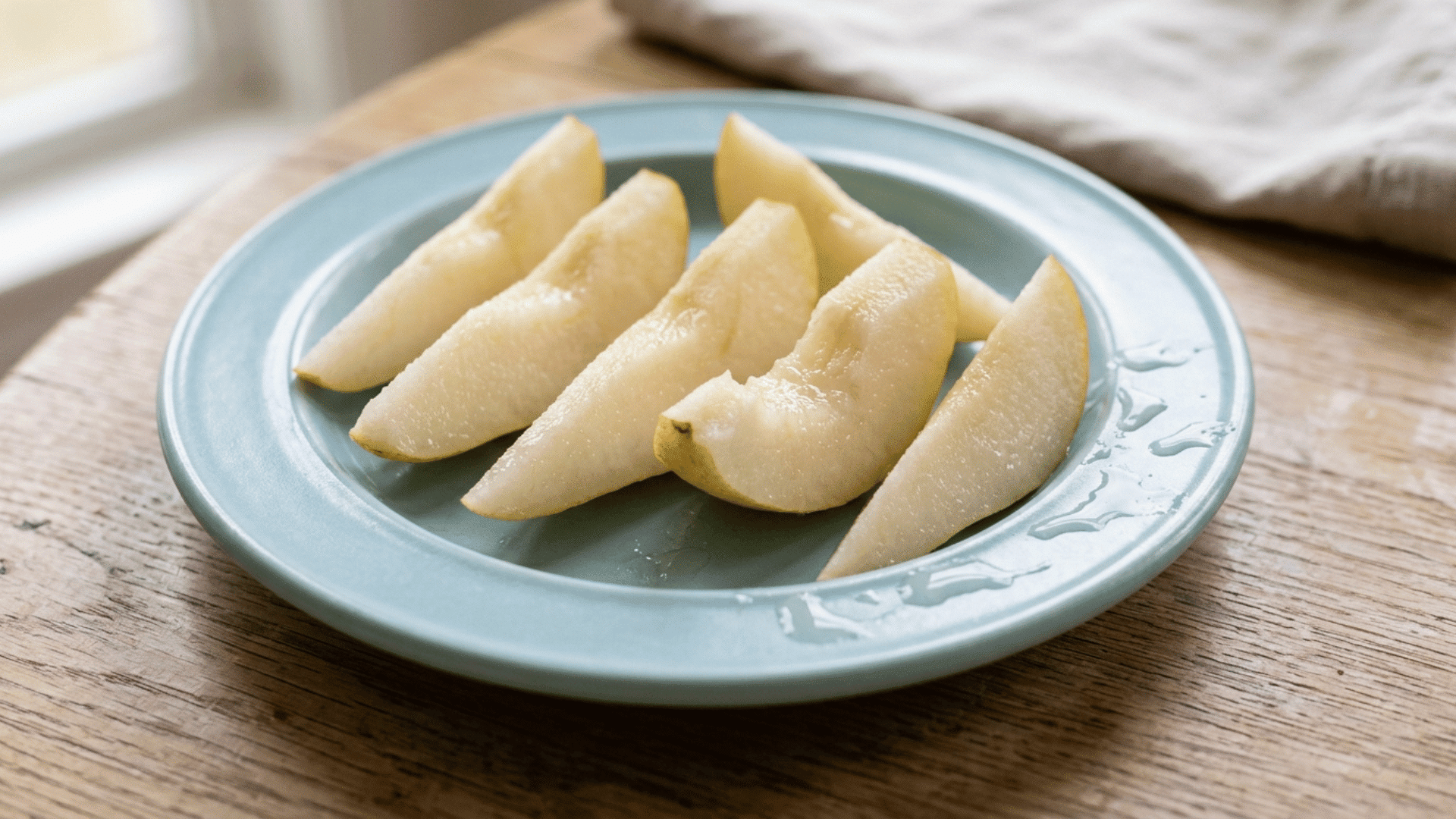 steamed pear spears served on a blue toddler plate as a soft baby led weaning food