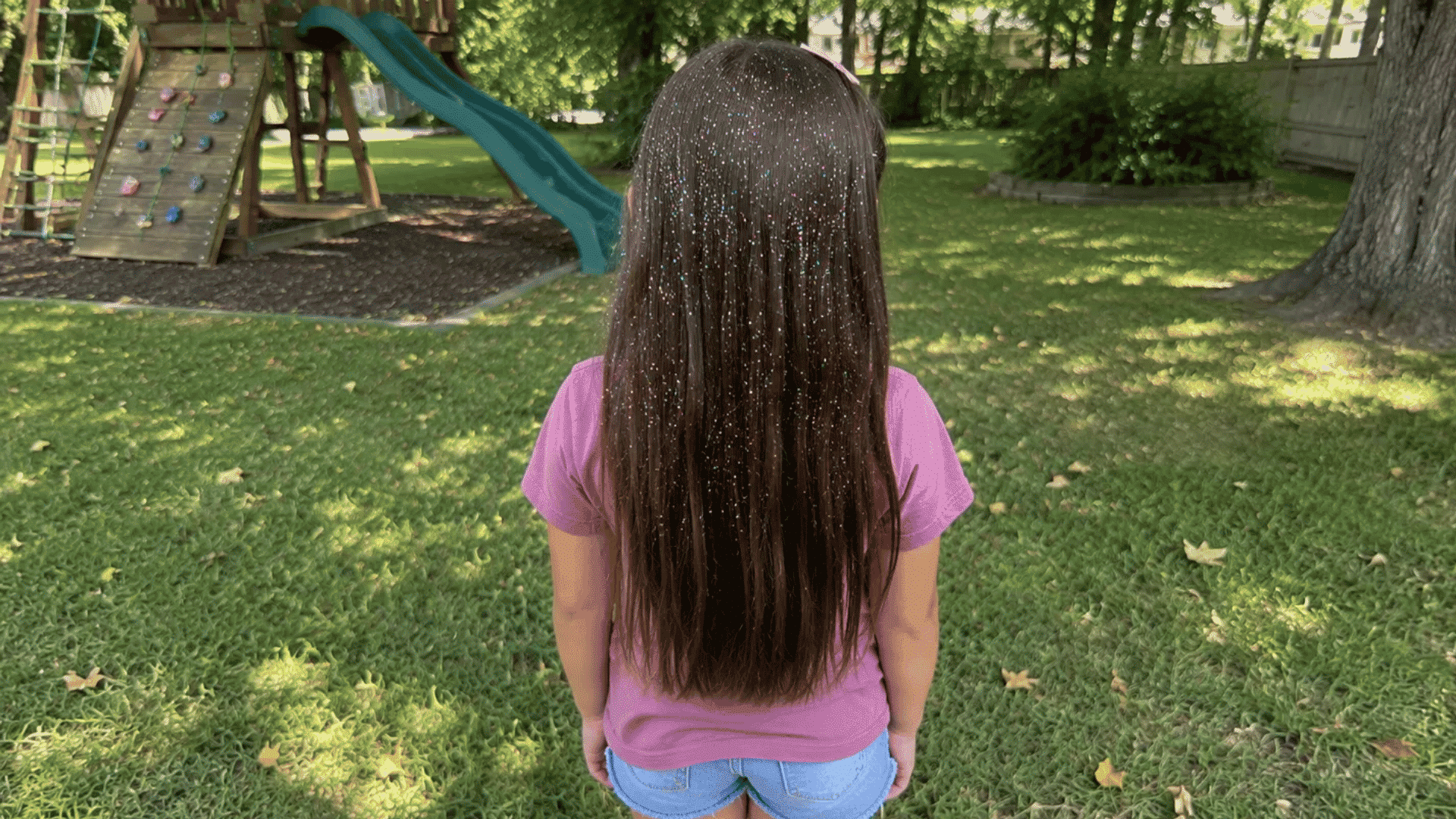 straight brown hair sparkling with confetti glitter spray in shaded backyard