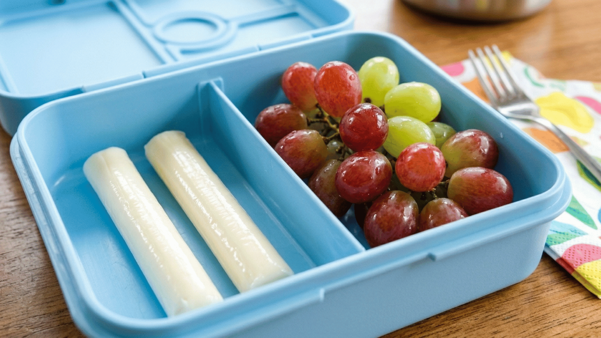 string cheese and grapes packed in a light blue plastic lunchbox
