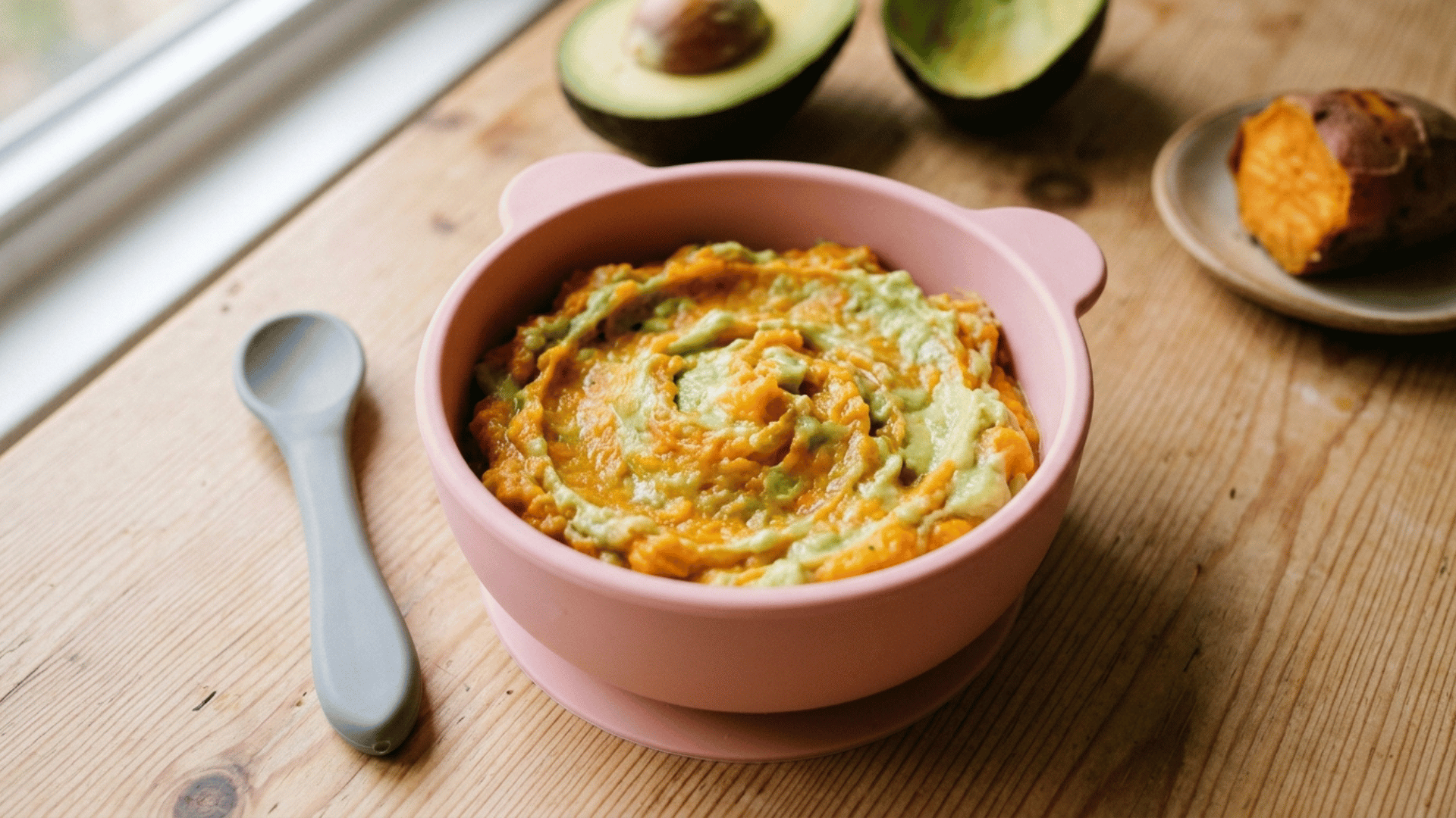 creamy sweet potato and avocado mash in a pink baby bowl with a baby spoon