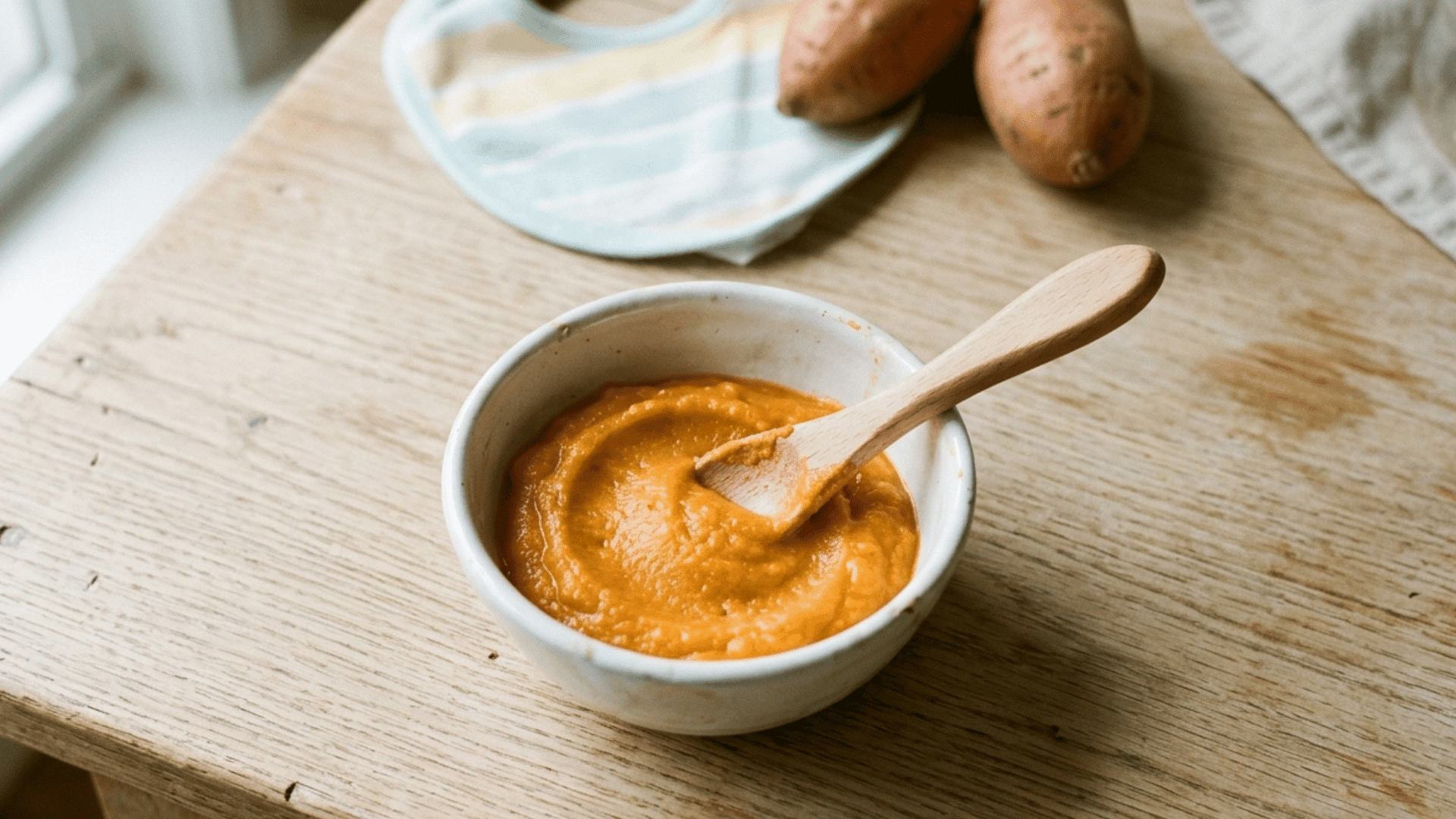 close-up of a bowl of smooth sweet potato baby food with a spoon on a wooden table