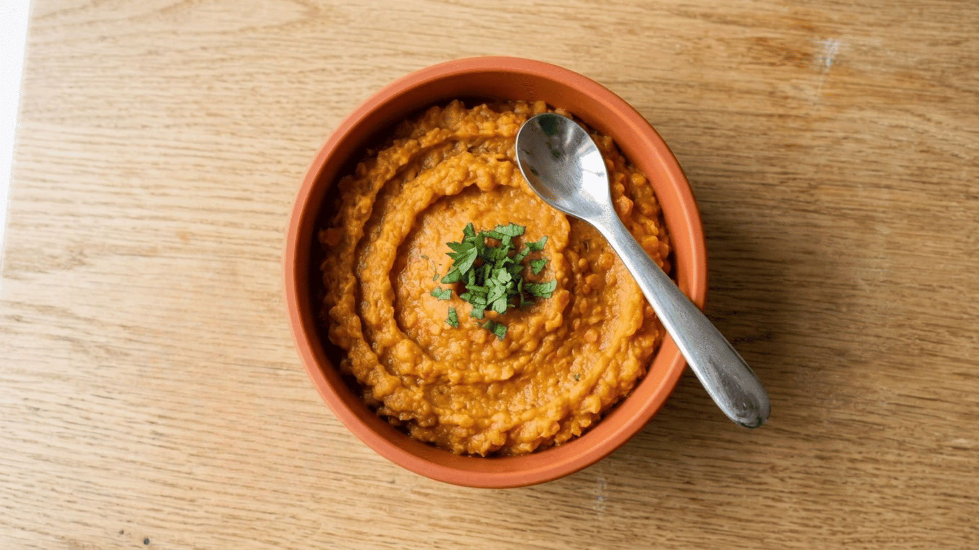 sweet potato and red lentil mash in an orange baby bowl