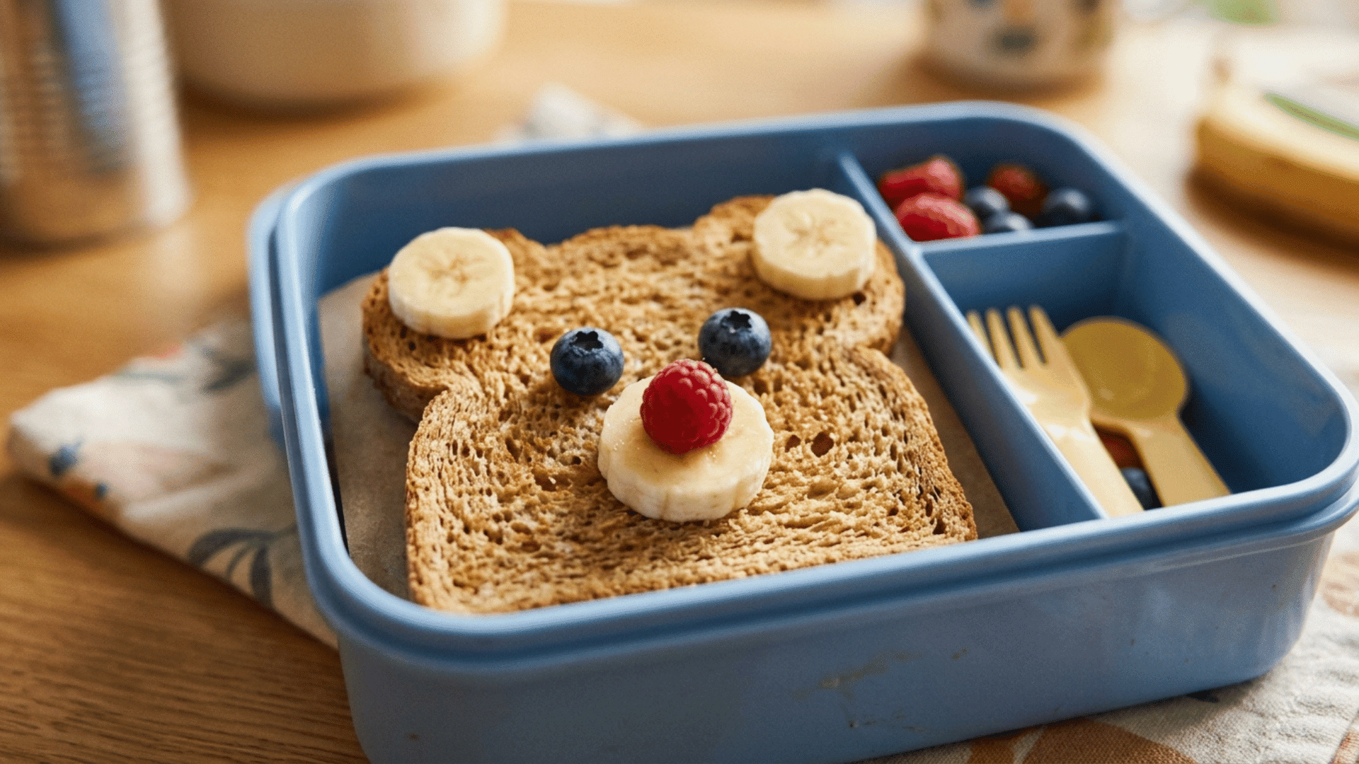 teddy bear toast with banana and berries packed in a blue lunchbox