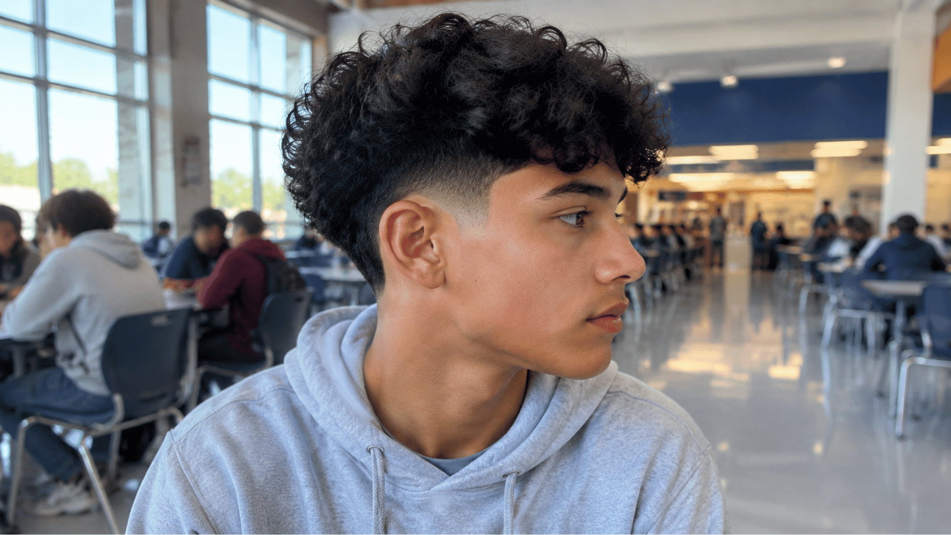 teen boy with curly top fade haircut showing natural curls and faded sides inside a modern coffee shop (1)