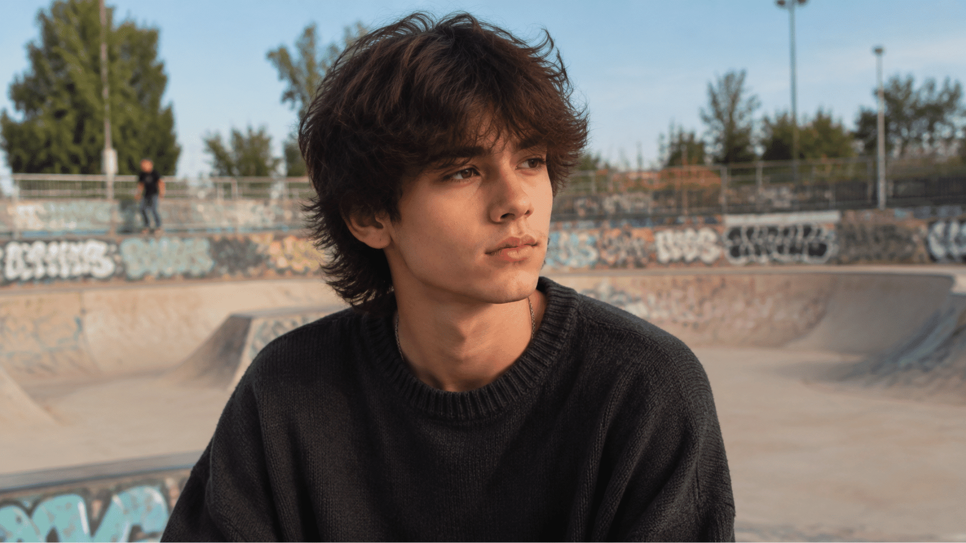 teen boy with shaggy layered haircut featuring messy textured layers while standing at an outdoor skate park