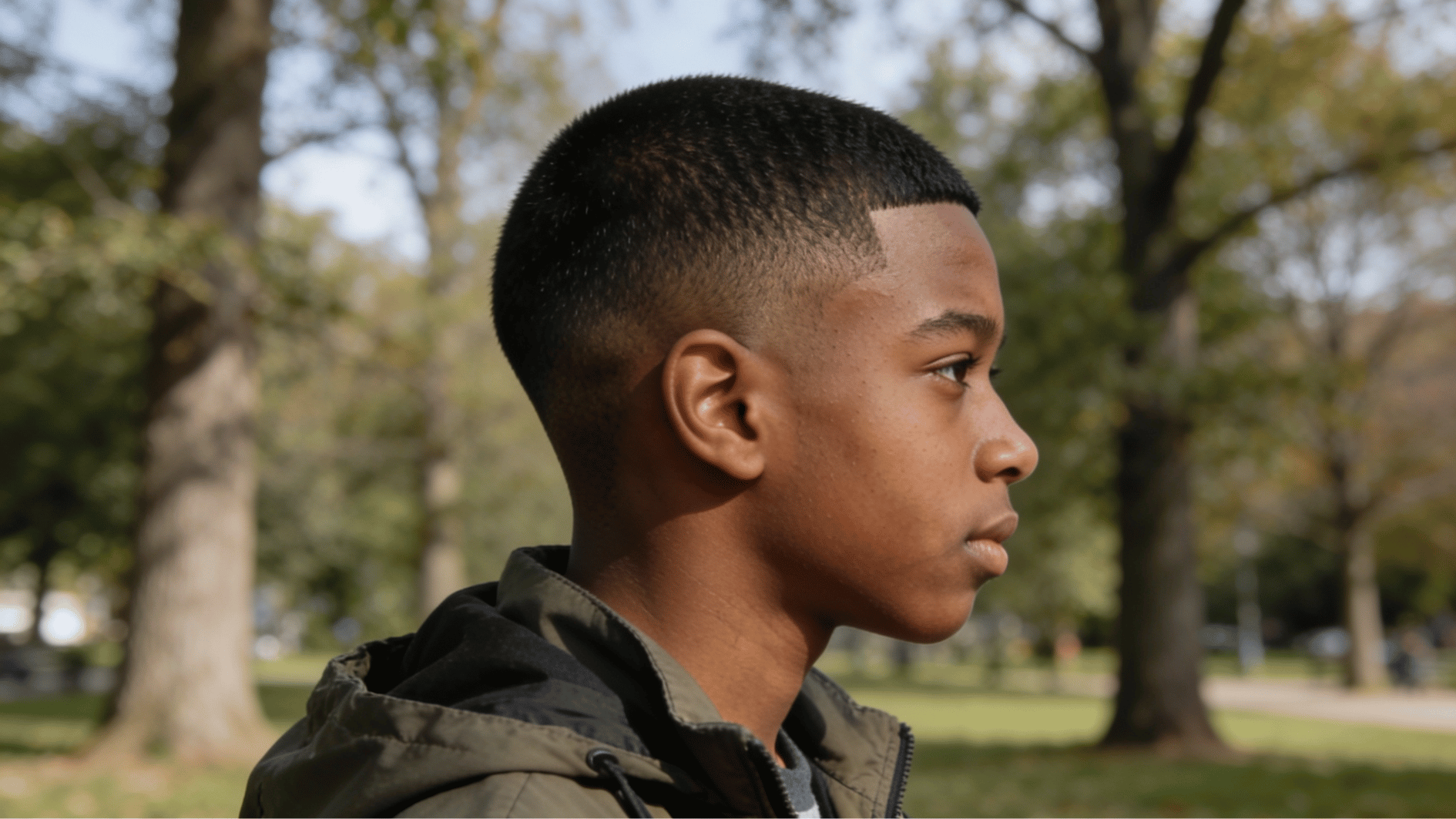 teen boy with simple buzz cut hairstyle showing evenly trimmed short hair while standing in an outdoor park