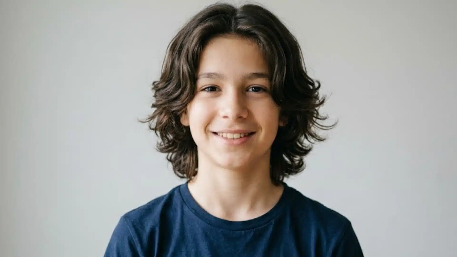 Teenage boy with a curtains haircut featuring medium length layered hair parted in the center with soft waves
