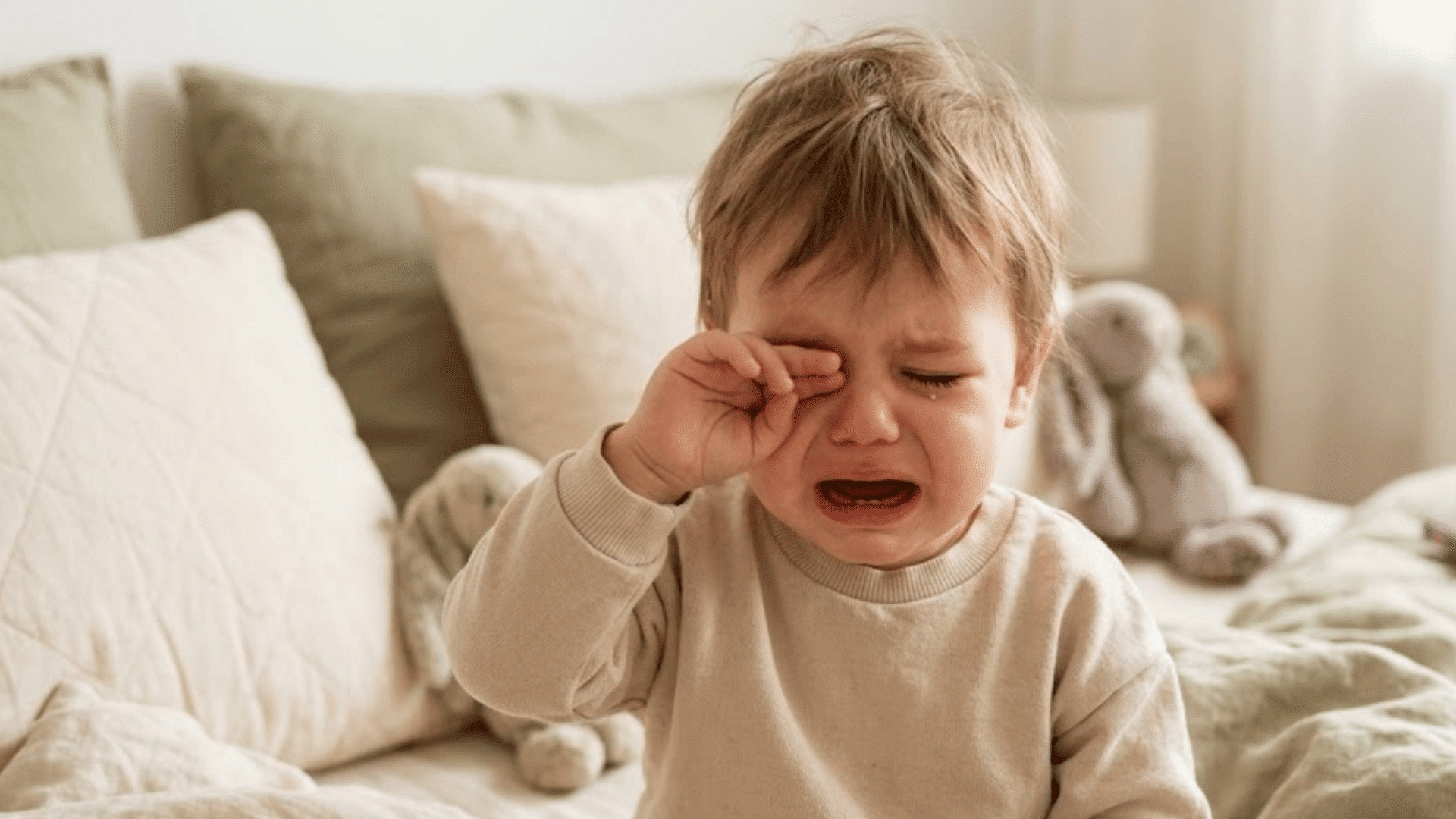 toddler crying after waking from sleep while rubbing eyes in a cozy bedroom setting