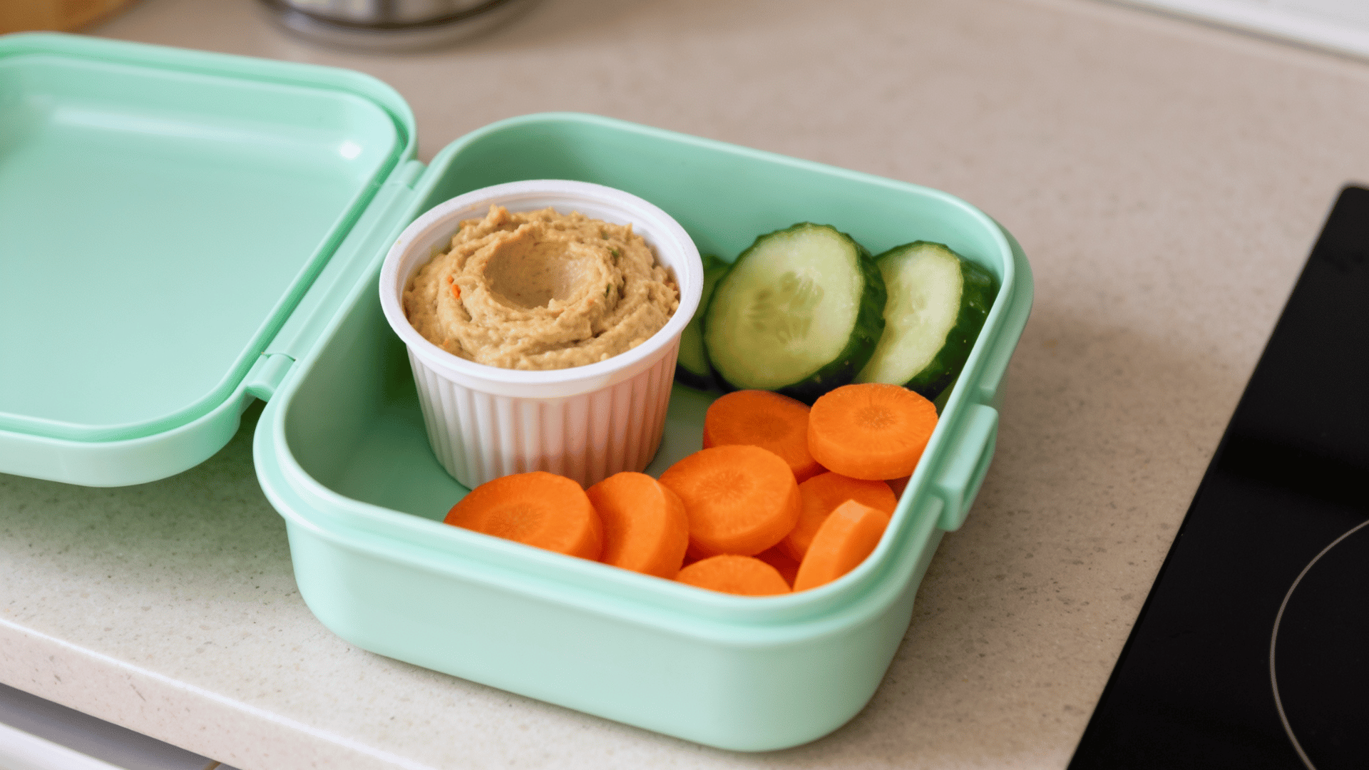 hummus cup with carrot and cucumber slices in a green kids lunchbox