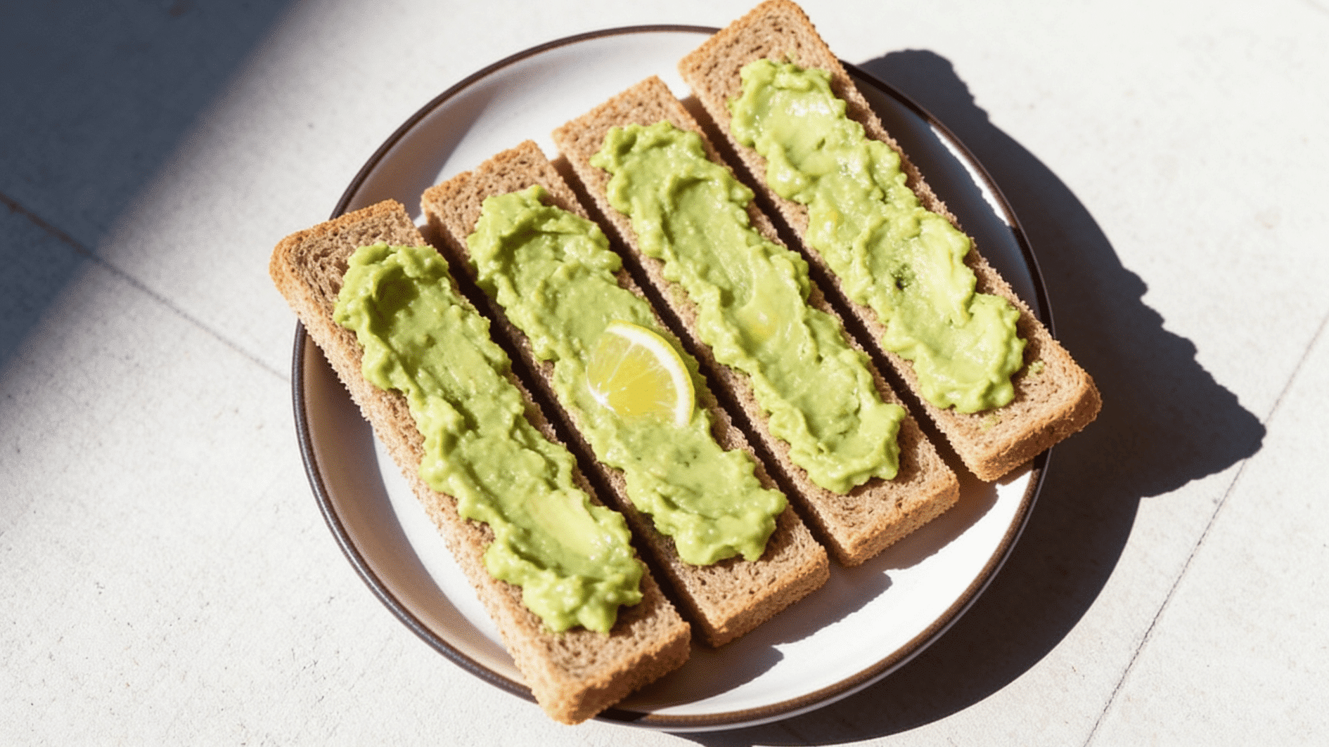 _whole-grain toast strips spread with creamy mashed avocado, tiny squeeze of lemon visible