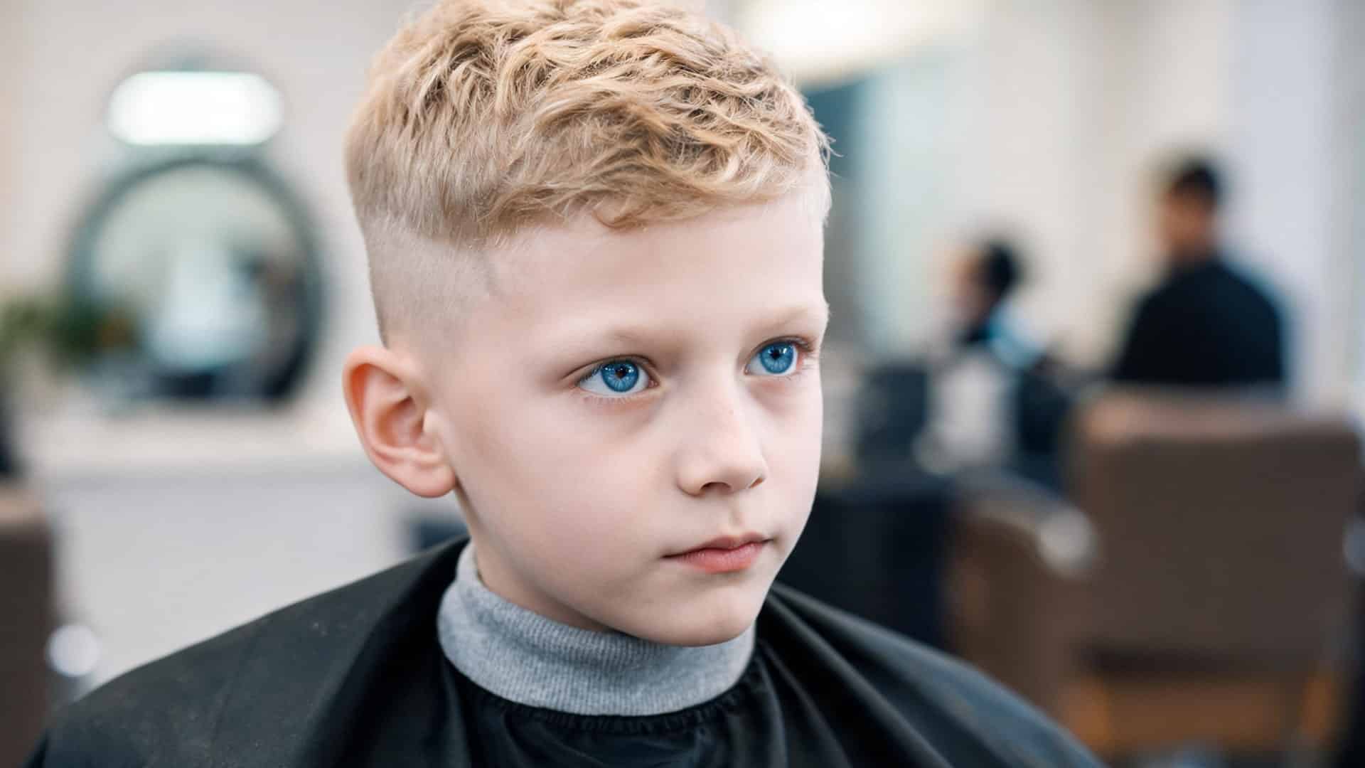 young boy with a textured crew cut featuring short wavy top and a clean low fade while sitting in a barber chair