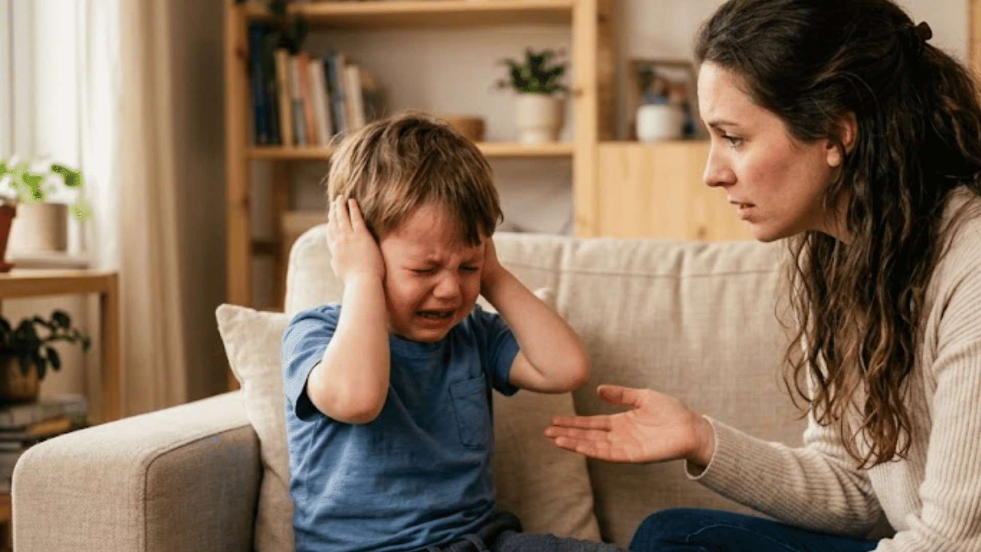 mother calmly talking to her crying three-year-old during a tantrum while sitting together on a living room sofa