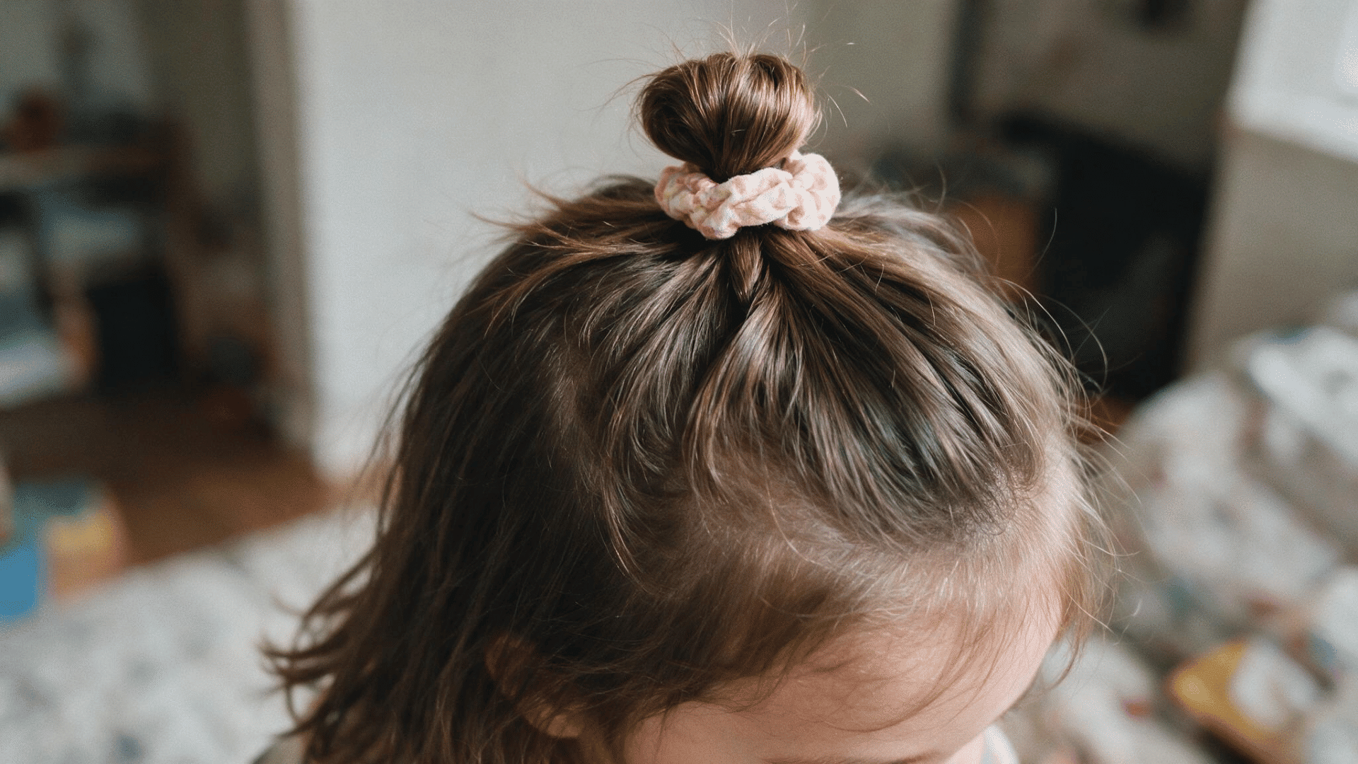 baby hairstyle with a half up top knot secured by a soft floral scrunchie in natural indoor light with a cozy home background