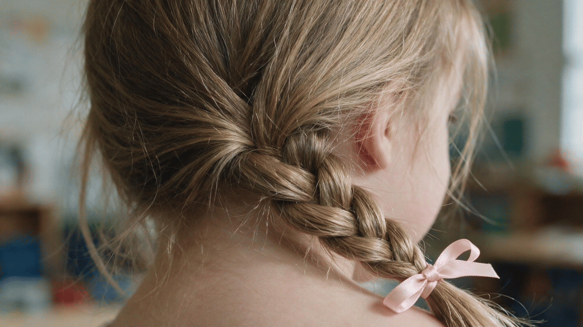 baby hairstyle with a loose side braid finished with a small pink ribbon viewed from the back in soft natural indoor lighting