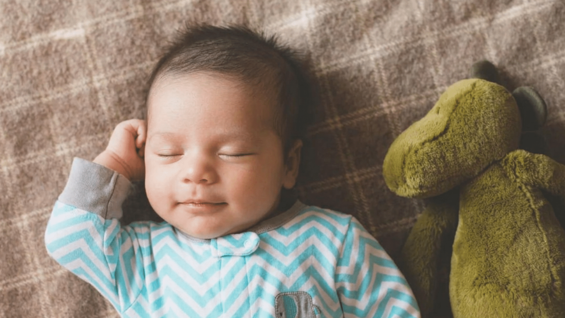 baby sleeping on a blanket beside a soft toy