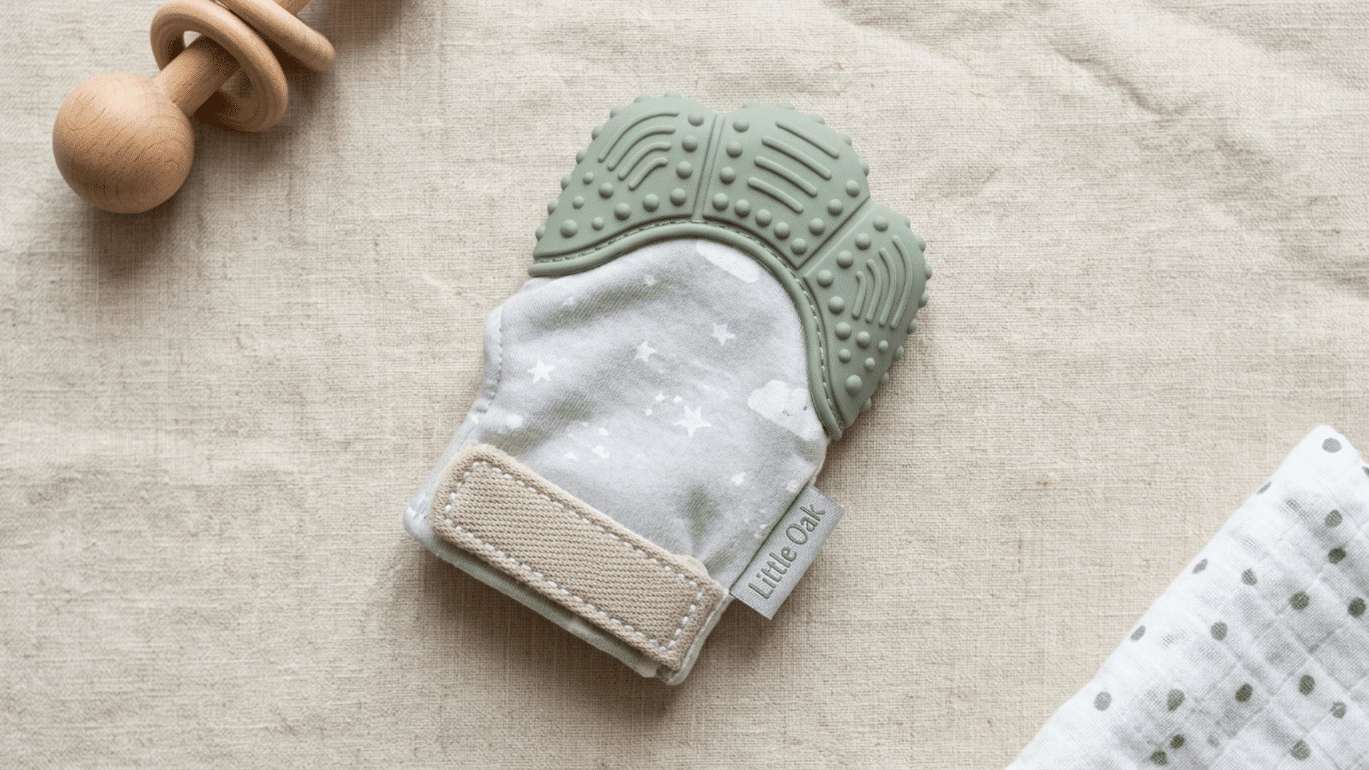 soft fabric baby teething mitten with a textured silicone top resting on a neutral cotton surface