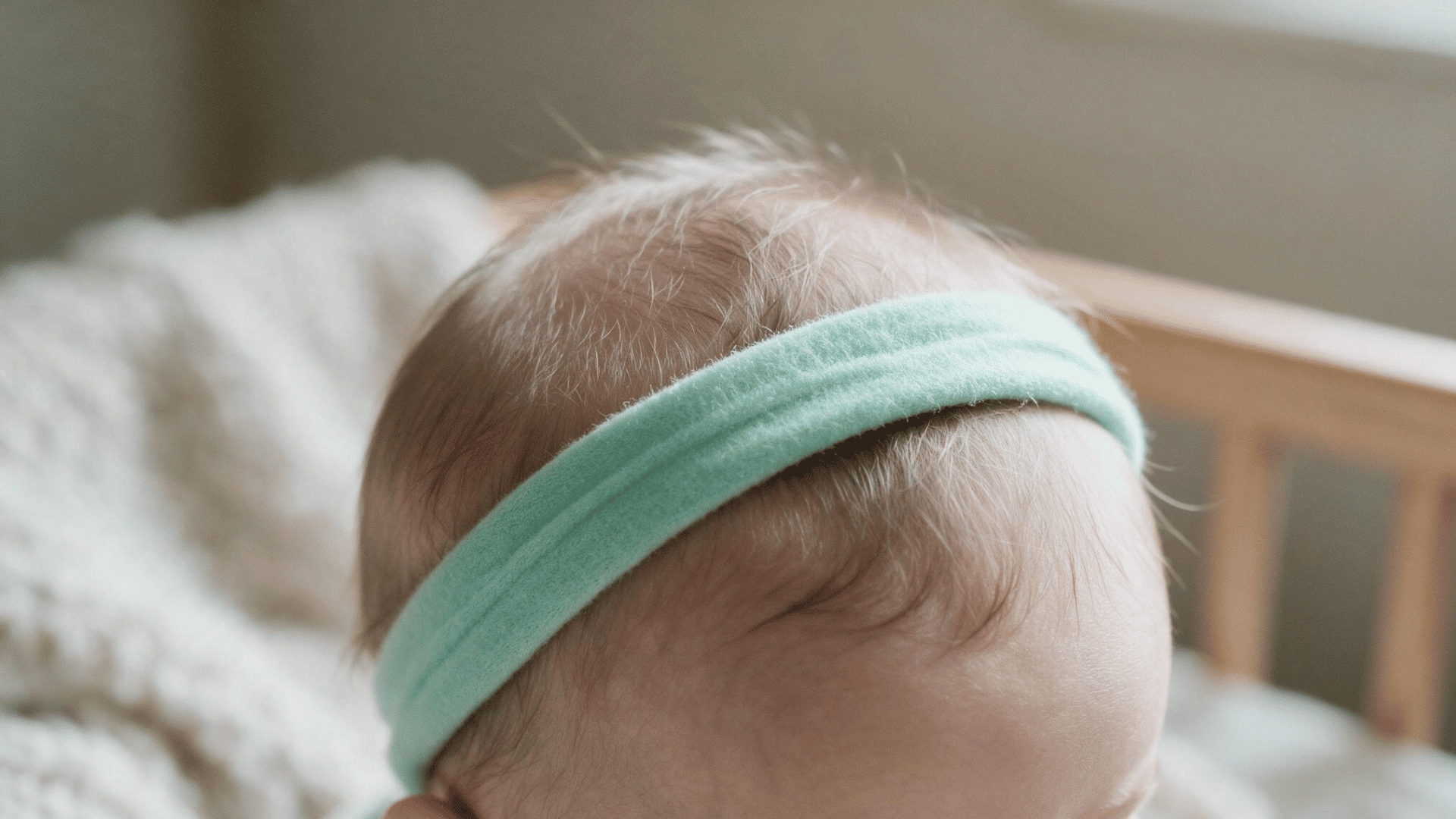 baby wearing a soft mint green headband on fine hair in natural indoor light with a cozy nursery background and close up view