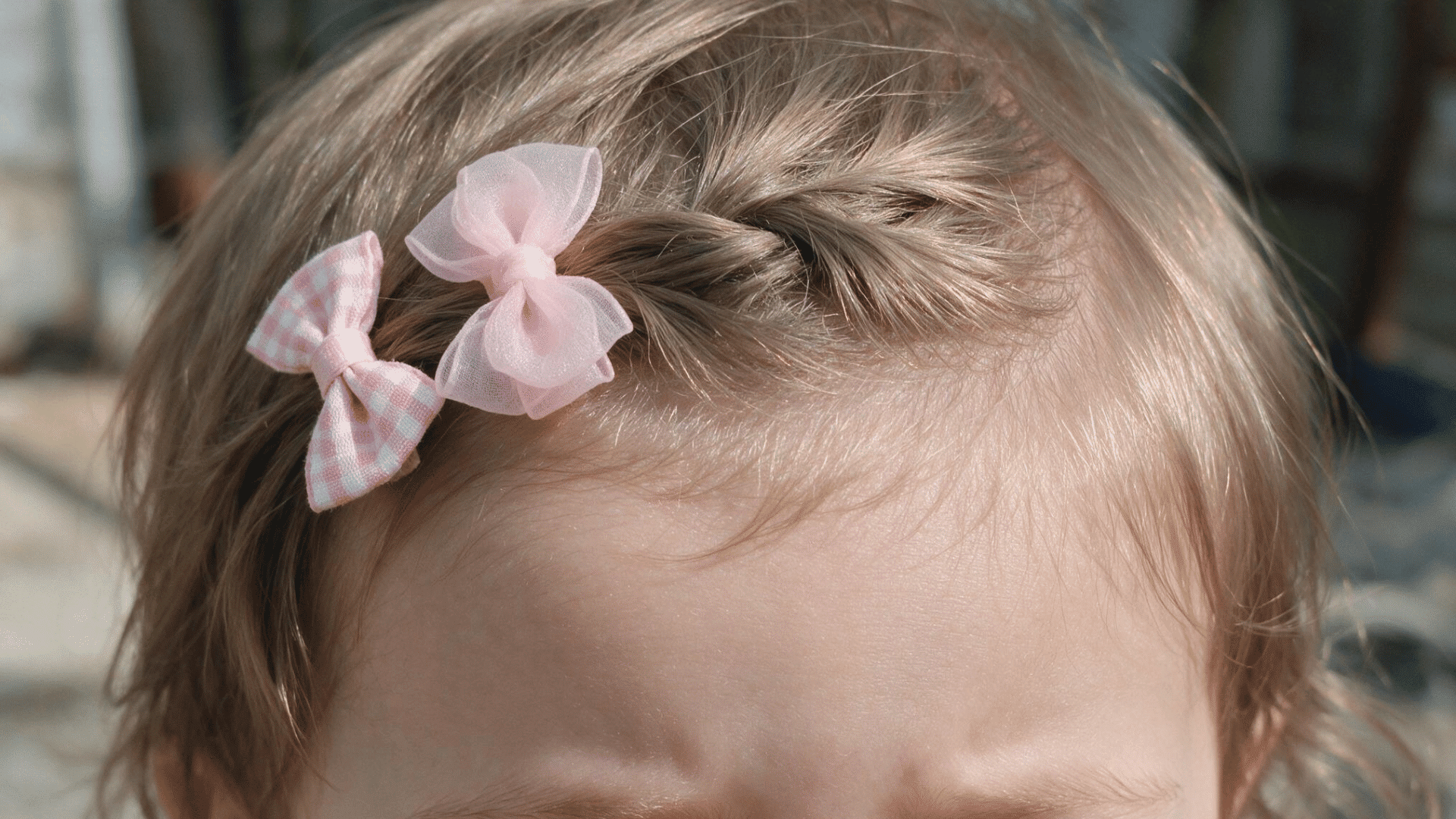 baby with a front twist secured by two soft pink bow clips on short hair in natural daylight with a close up front view