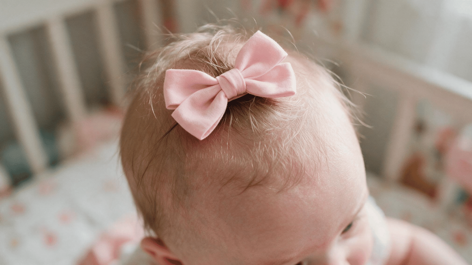 baby with fine hair wearing a soft pink bow clip on top of the head in a bright nursery bedroom
