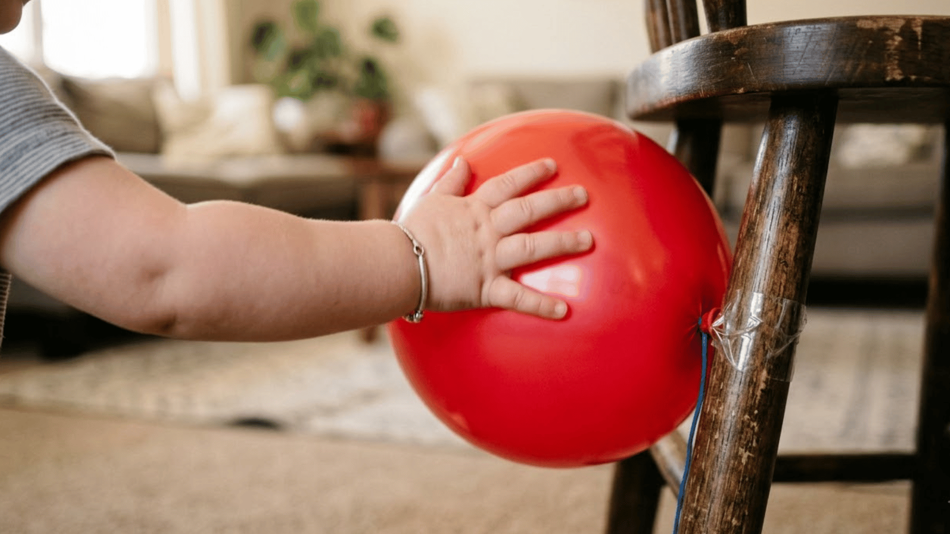 toddler hand bats an open palm at a balloon taped to a wooden chair