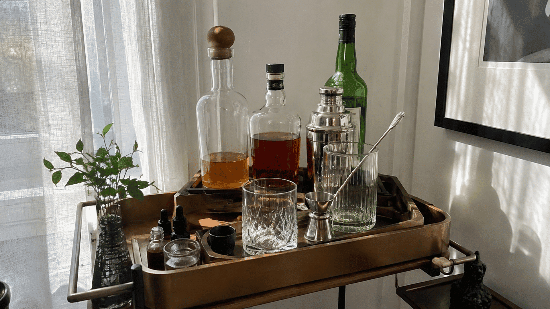 Bar cart with layered brass trays holding whiskey bottles, cocktail shaker, jigger, bitters, and crystal glassware