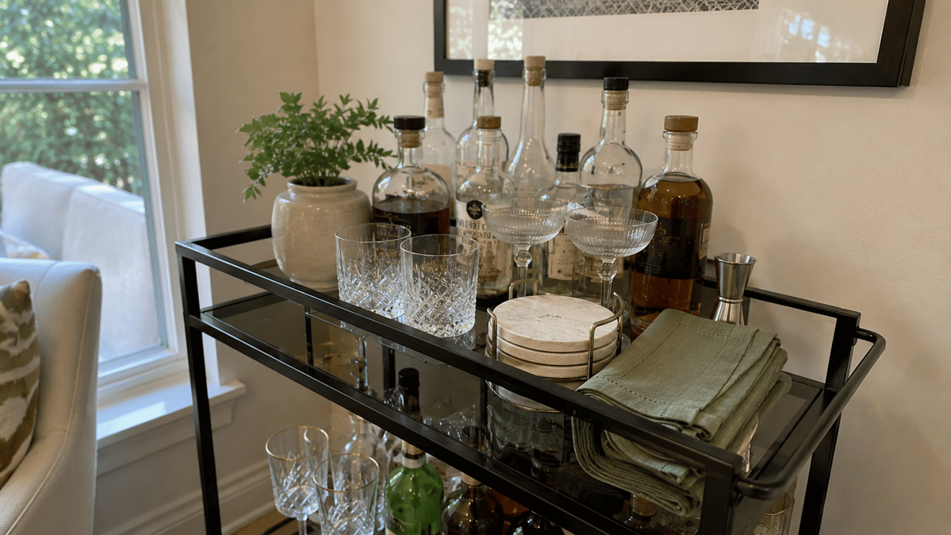 Black bar cart with whiskey bottles, crystal glasses, stacked marble coasters, and folded green cloth napkins