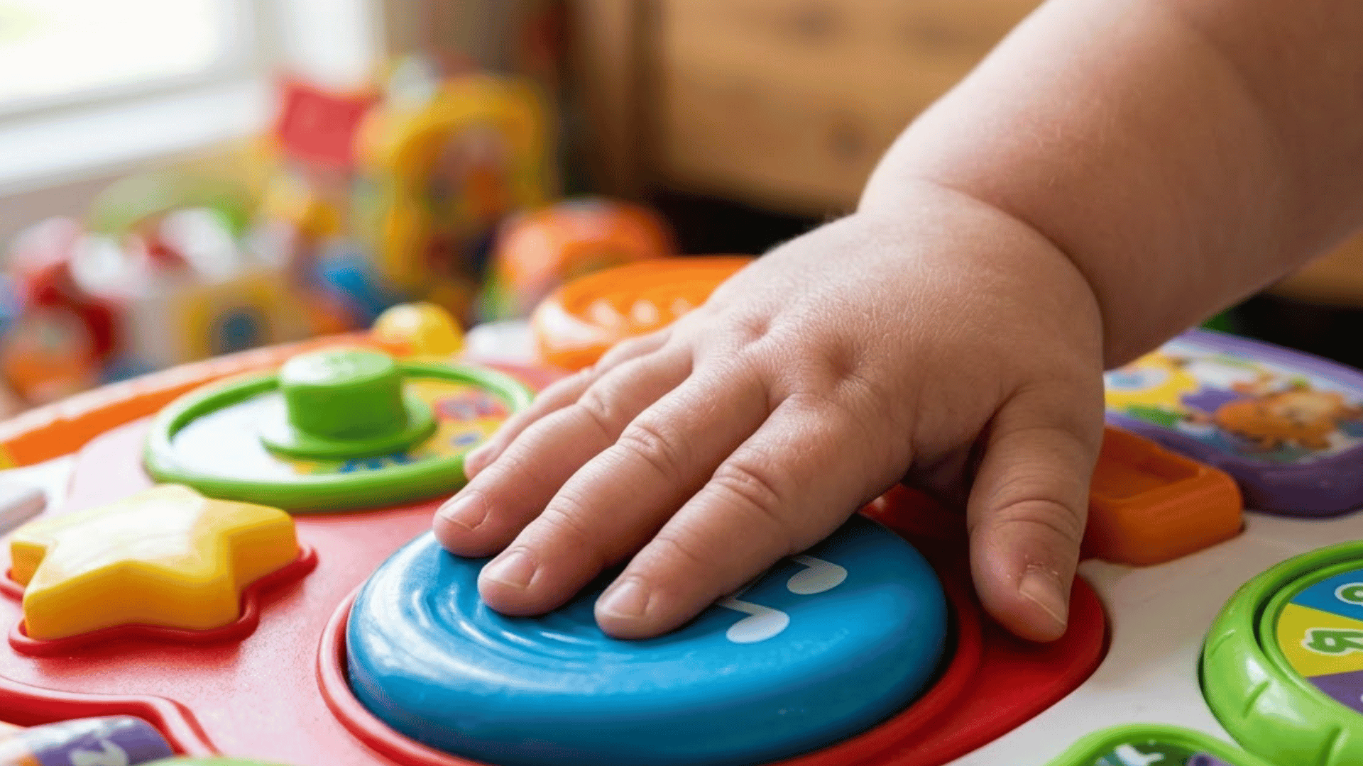 toddler finger presses flat against a large button on a colorful activity toy
