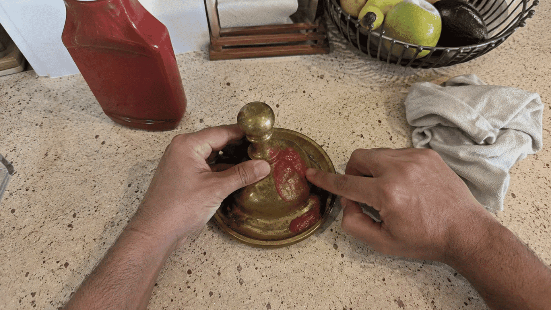 finger spreading ketchup over a tarnished brass bell on a kitchen counter