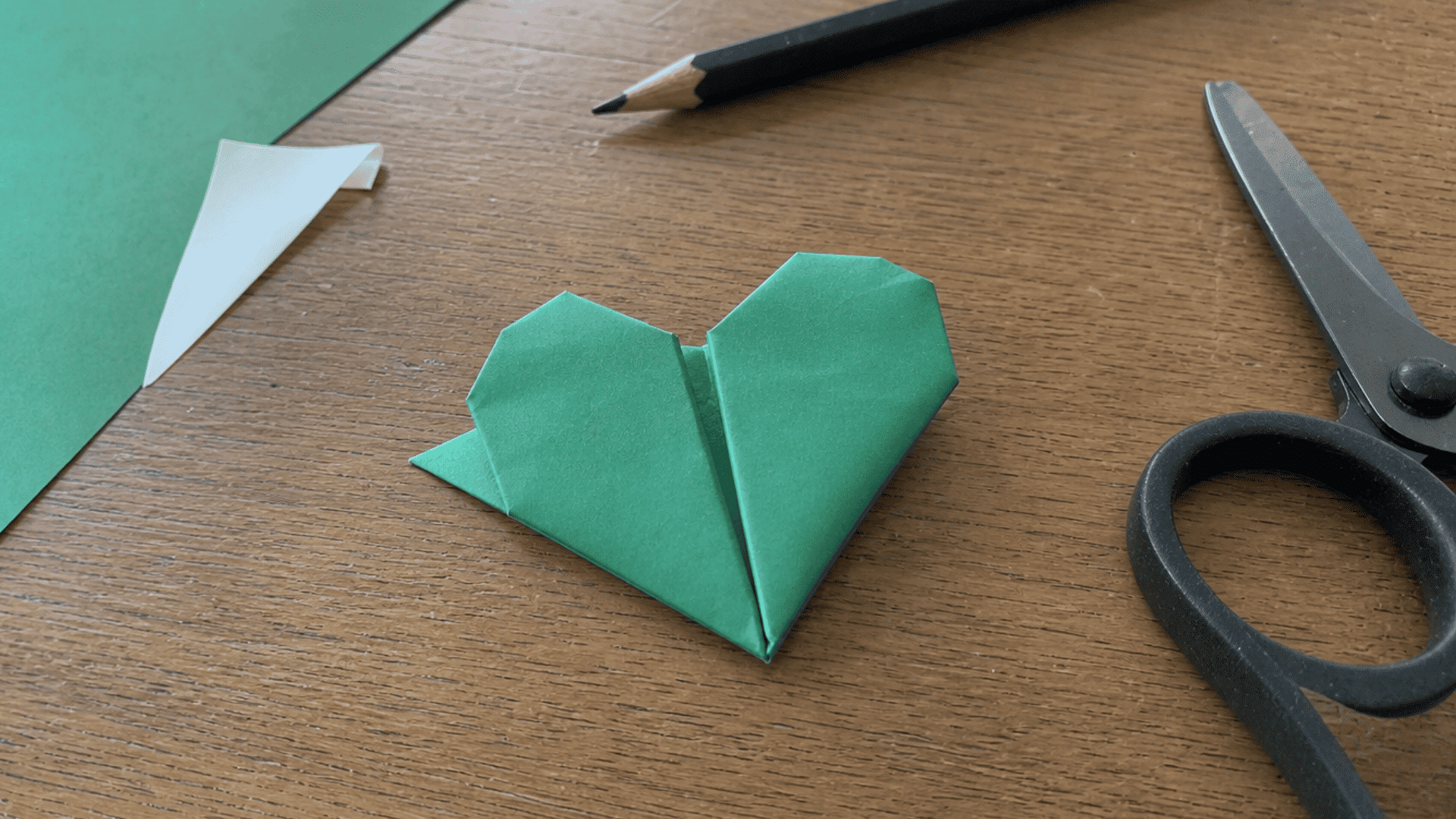 green folded paper heart with two connected heart sections on a wooden craft desk