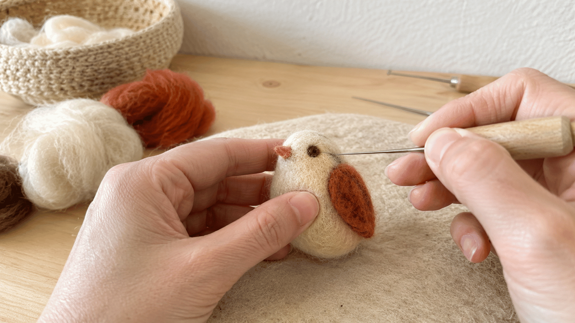 Hands adding fine eye and detail work to a small felted bird with wing