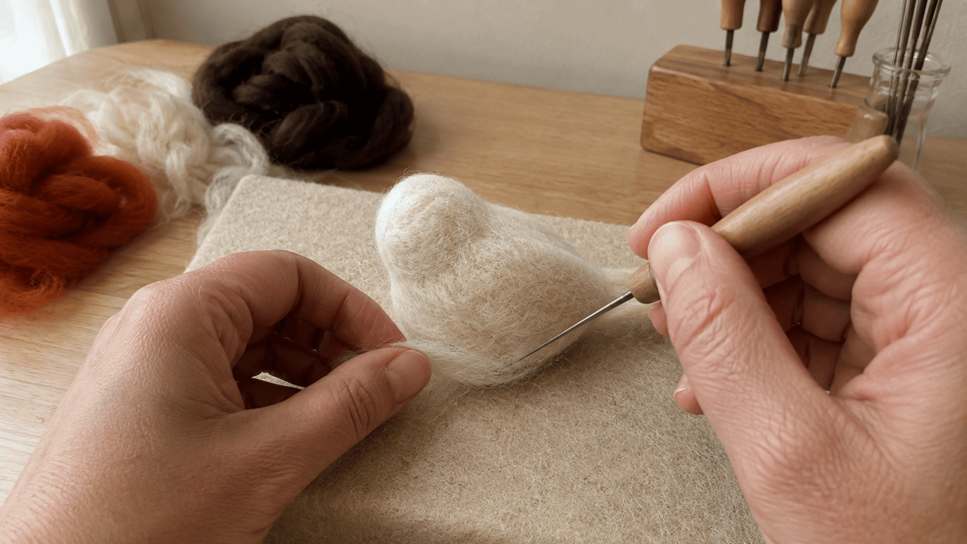 Hands felting a raised wool bump onto a rounded bird-shaped base with a needle