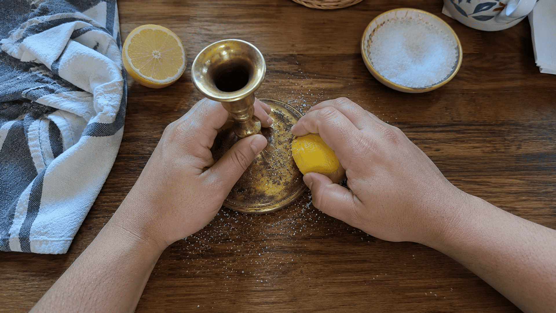 hands rubbing a salted lemon half over a tarnished brass candlestick