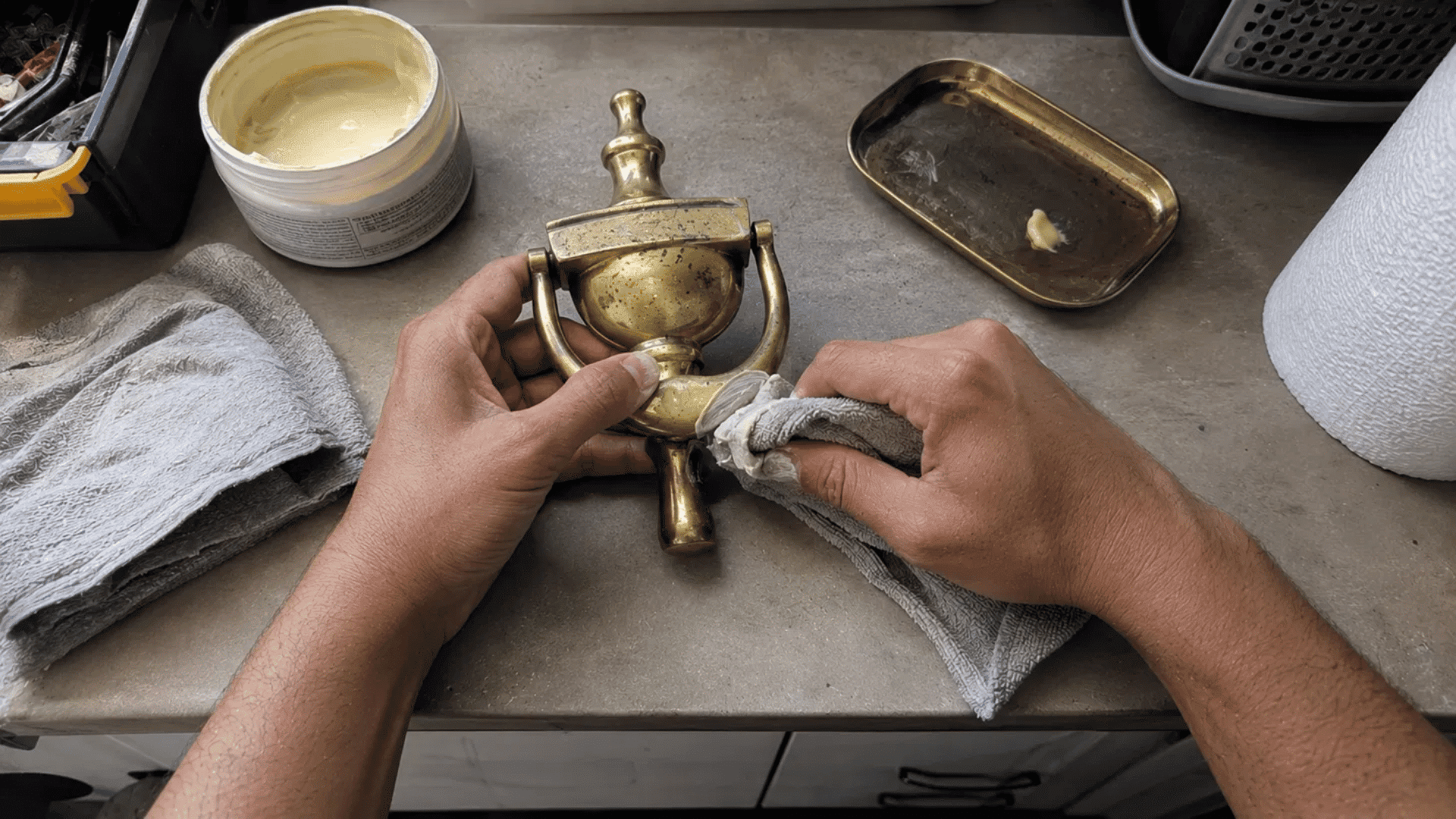 hands rubbing commercial brass cleaner onto a brass door knocker with a cloth